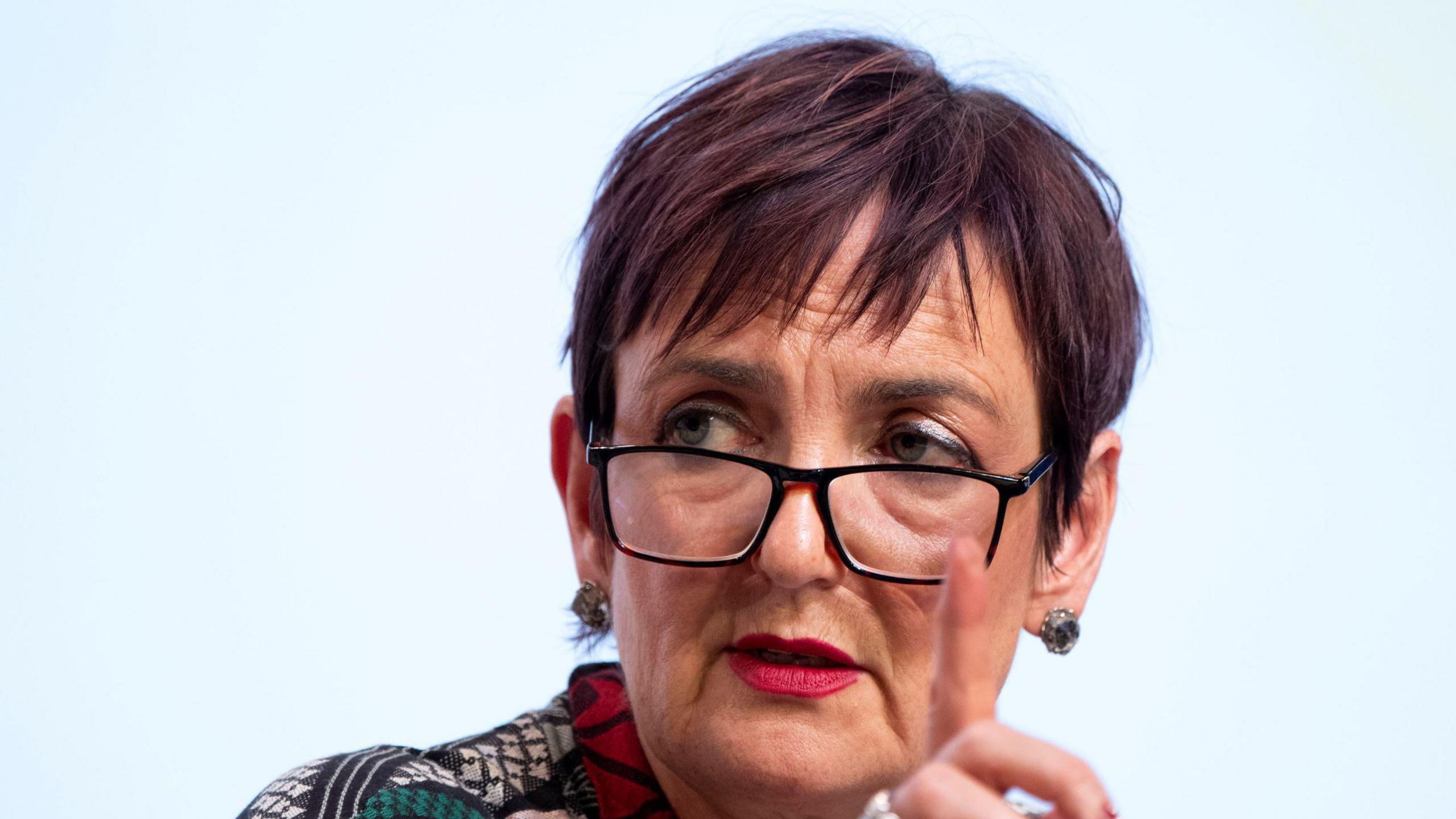 Head shot of Angela Constance, wearing glasses and with a hand raised, suggesting she is raising a point 