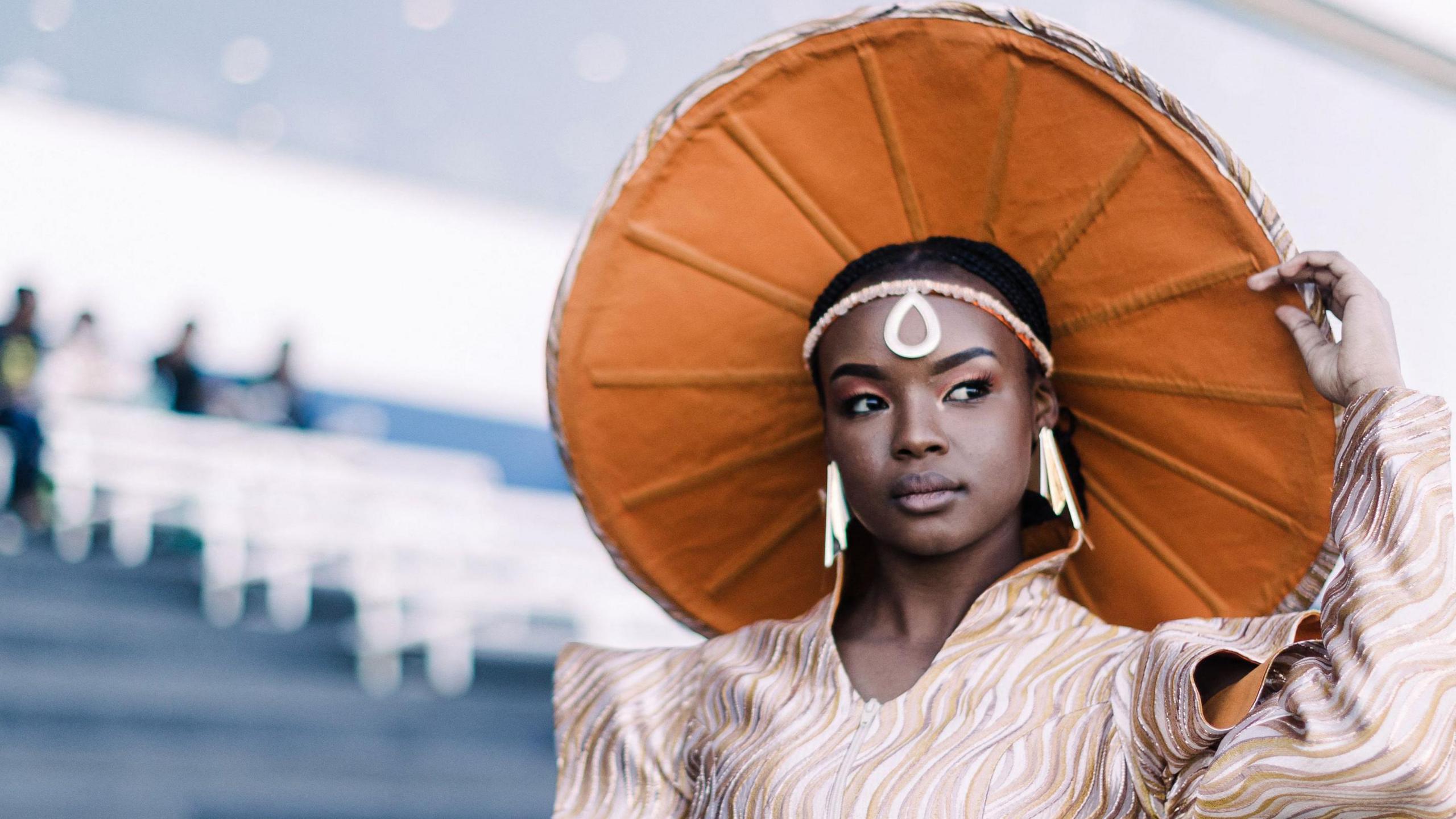 A woman wears a large circular headpiece. The underside is a burnt orange colour.