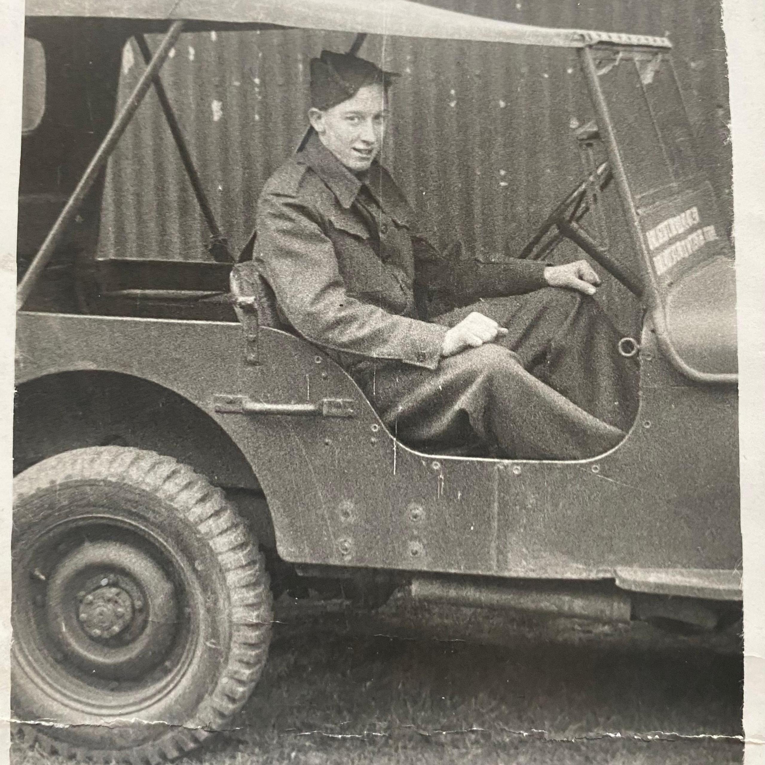 An old black and white photo of a young man in army uniform driving an old army jeep.
