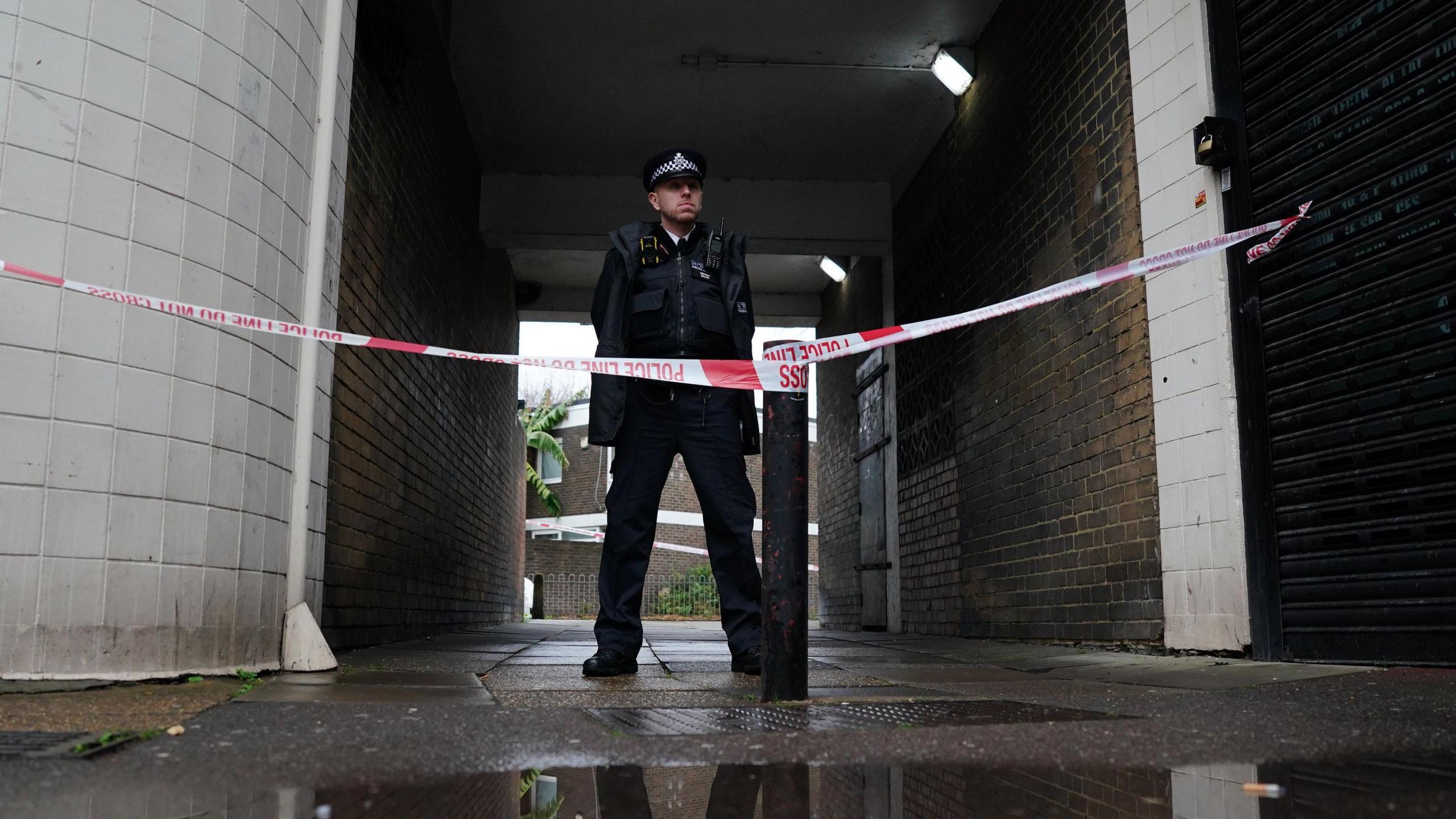 Police officer and police tape outside the block of flats where a 22-year-old woman was stabbed to death in a fight with a 16-year-old boy