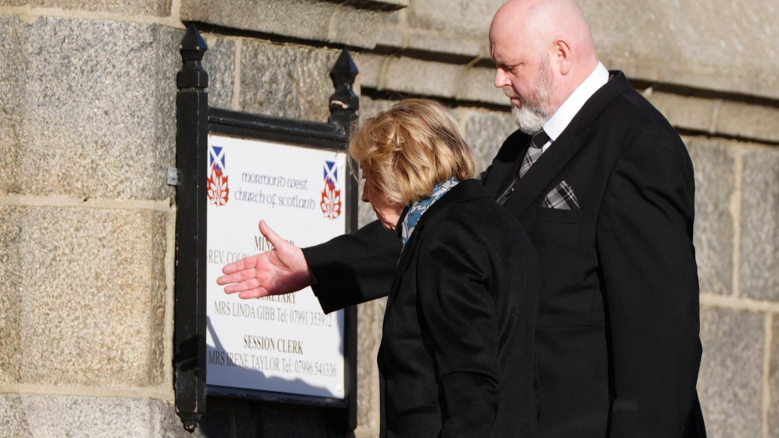 Alex Salmond's widow Moira is directed into the church by a man wearing a black suit