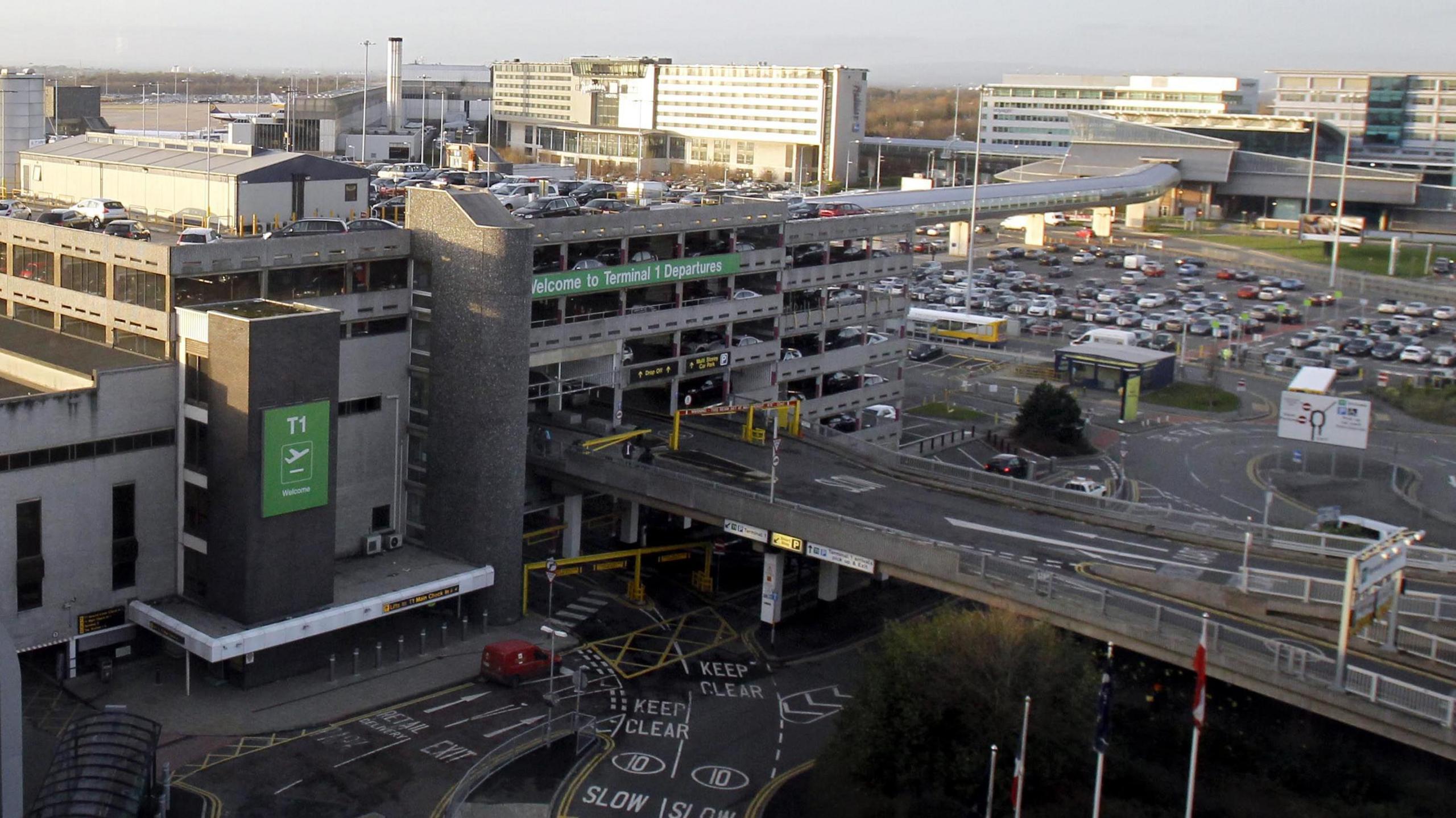 Roads close to Terminal One at Manchester Airport, including the entrance to the pick-up and drop-off zones. Car parks and airport hotels can be seen in the distance.