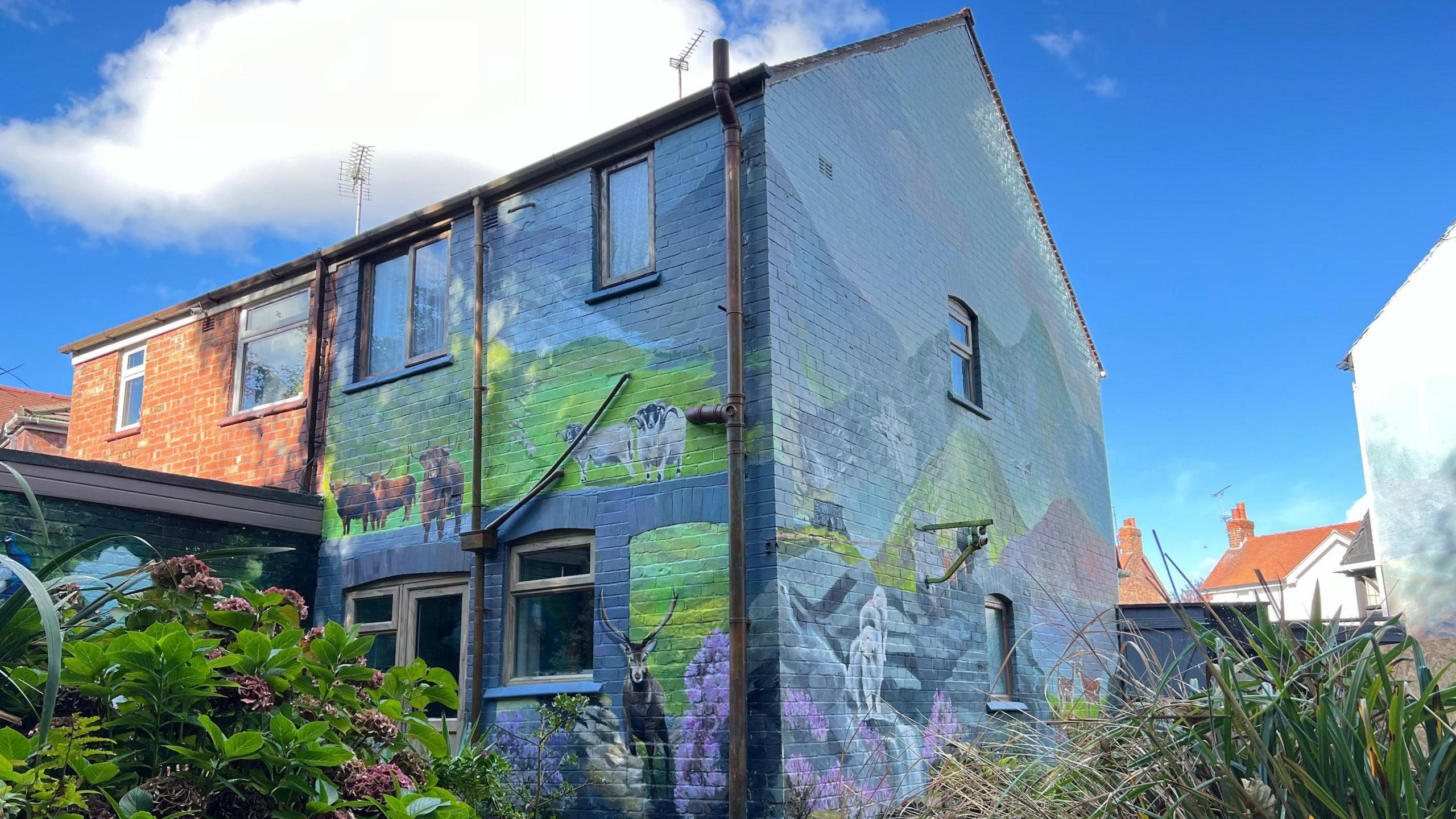 The mural Robert painted on his house which shows cows and sheep against the lake district mountains 