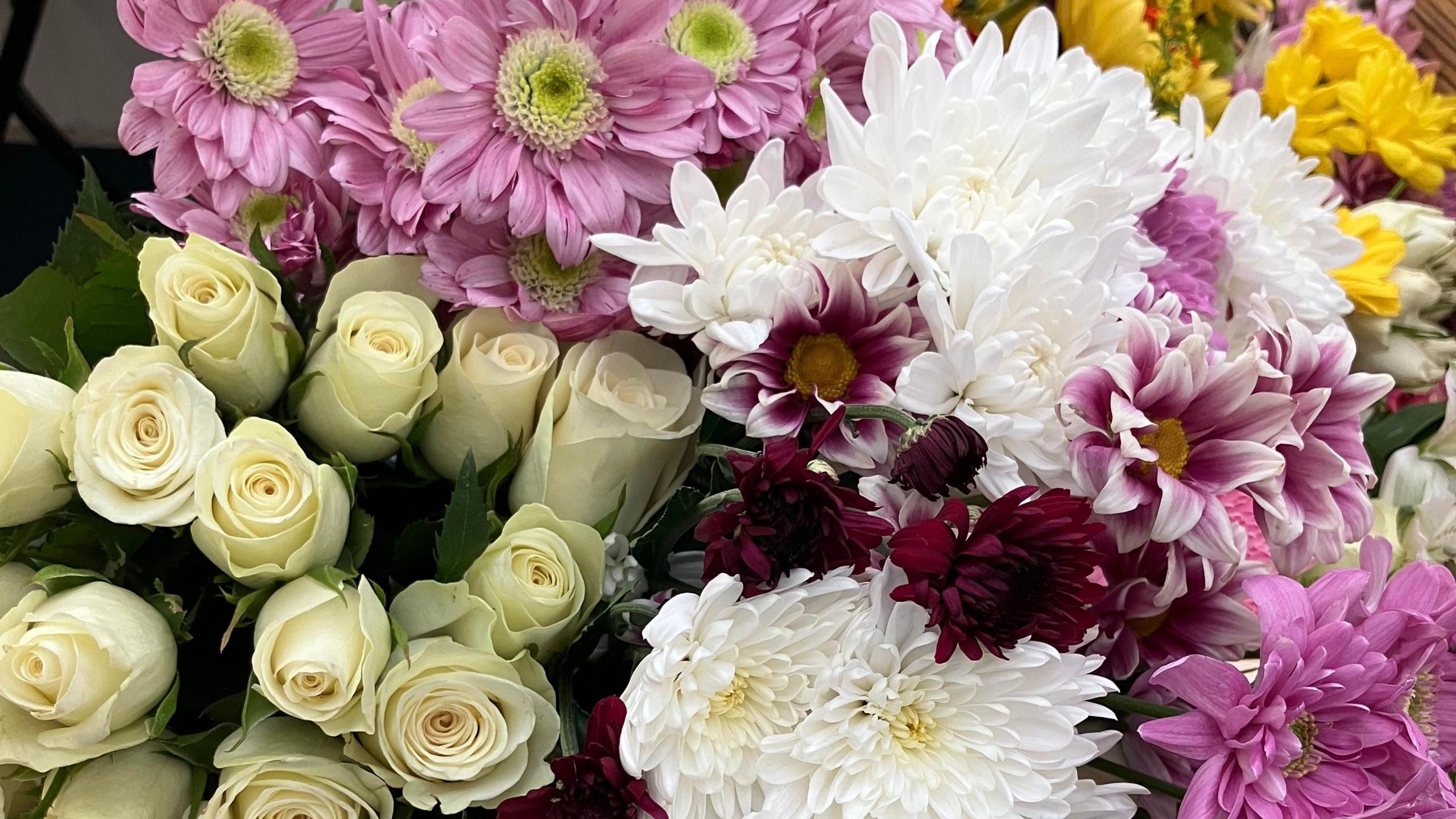 Bouquets of flowers left in tribute to Liam Payne at Clevedon Pier. Cream roses, pink, white, burgundy and yellow flowers can be seen. 