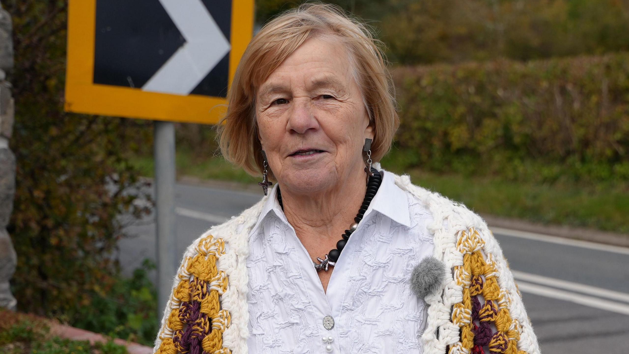 Dynes yn gwisgo cardigan frown dros grys gwyn yn sefyll o flaen ei chartref yn Nhalerddig.