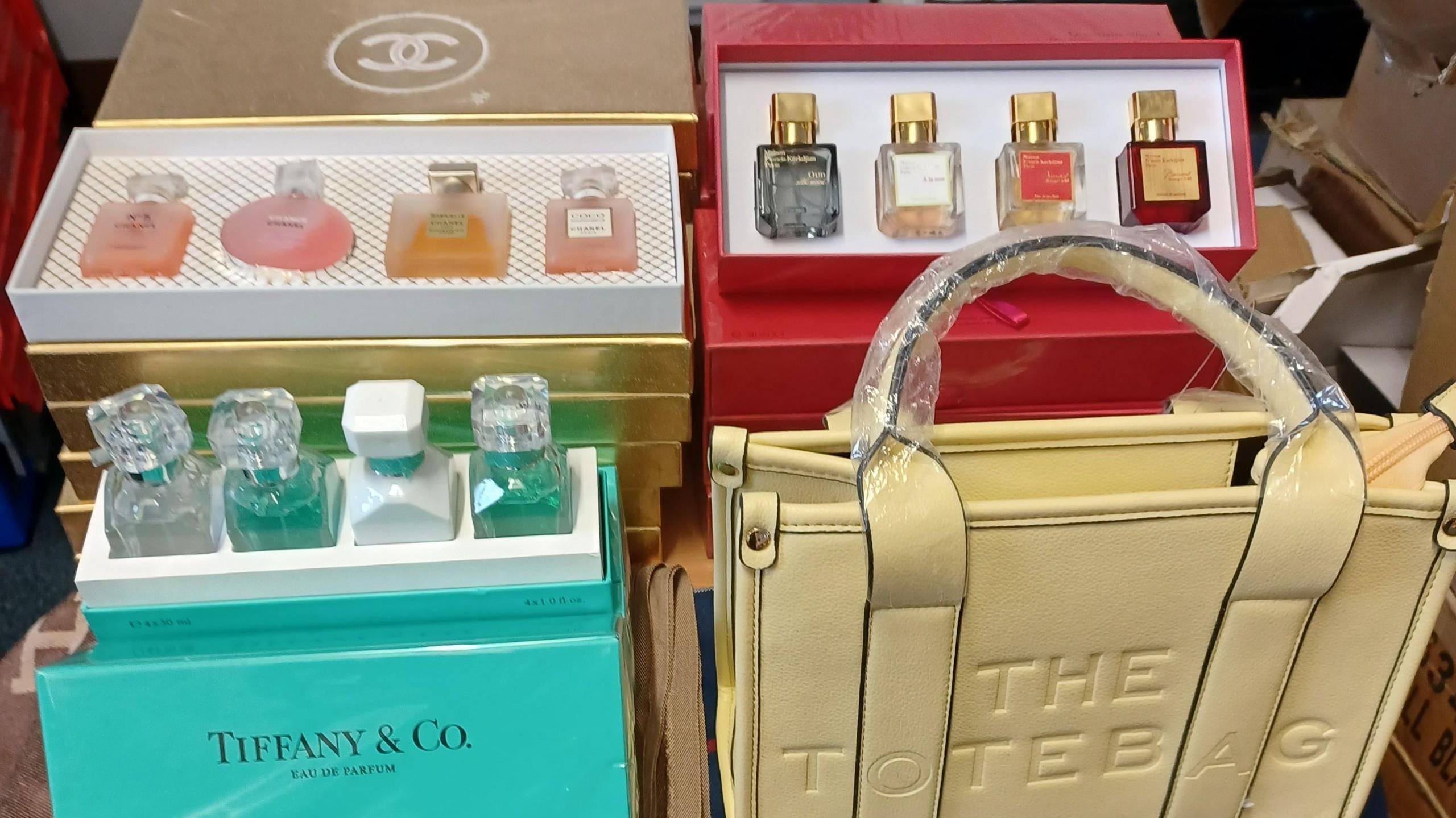 Fake Chanel and Tiffany perfume in boxes on a table along with a fake Marc Jacobs tote bag.