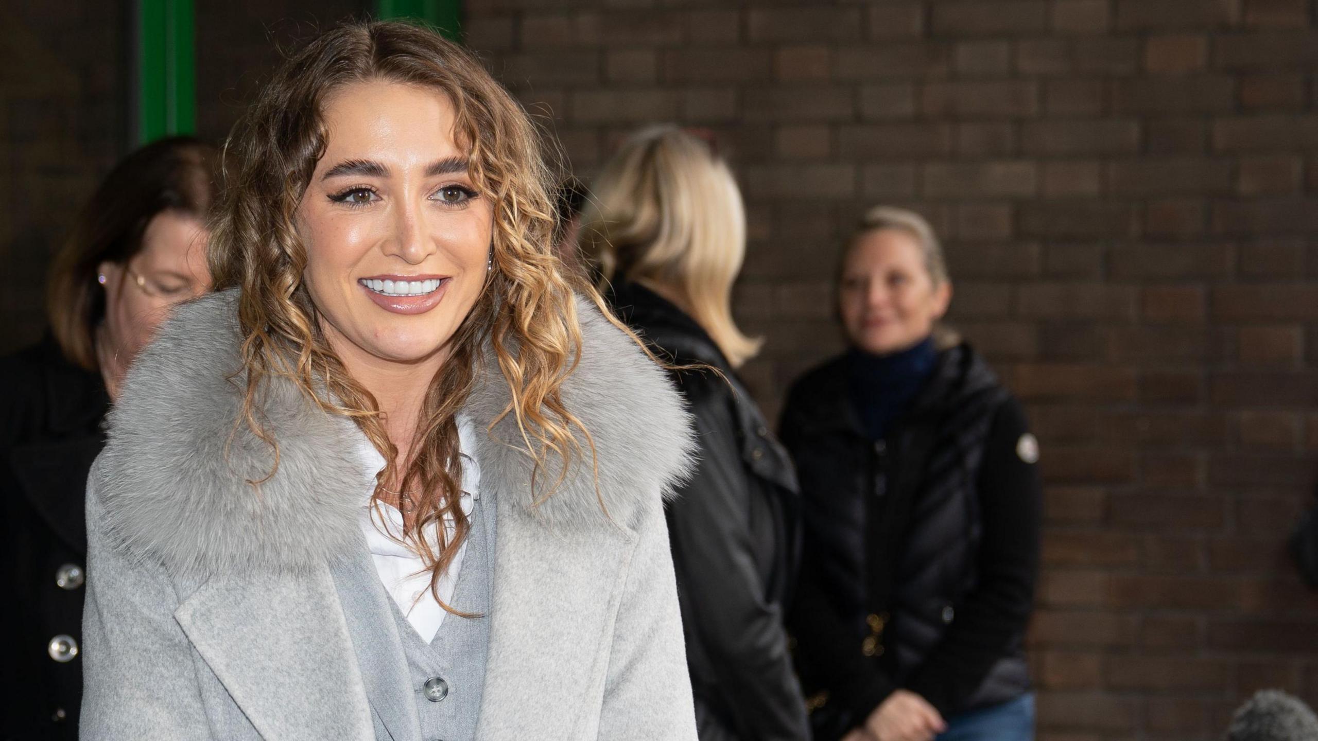 Georgia Harrison wears a grey coat with fur collar as she speaks to waiting press outside court