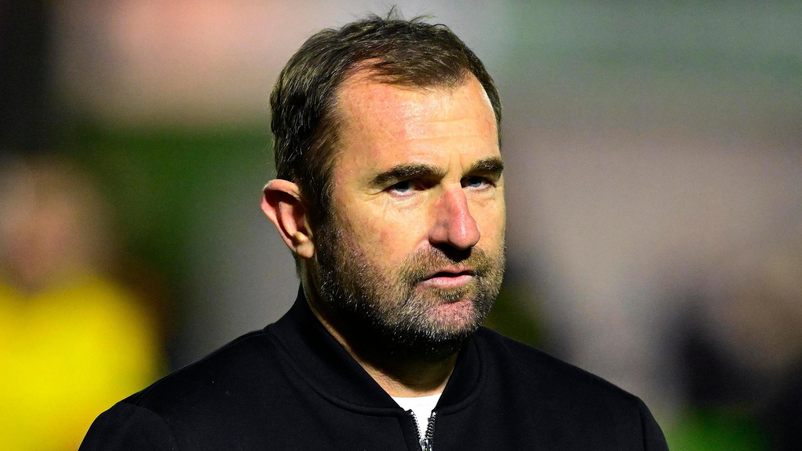 Paul Wotton, wearing a dark jacket on top of a white tee-shirt, looks straight ahead