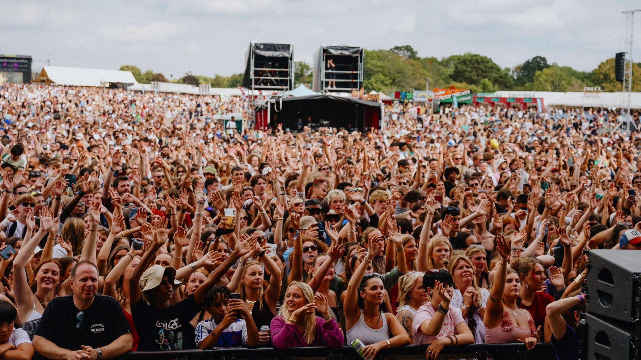 A view out from the main stage at Forwards Festival in Bristol, showing a huge crowd with many of them with their arms in the air and cheering or singing. It is a dry, clear summer day and many of the people are in T-shirts