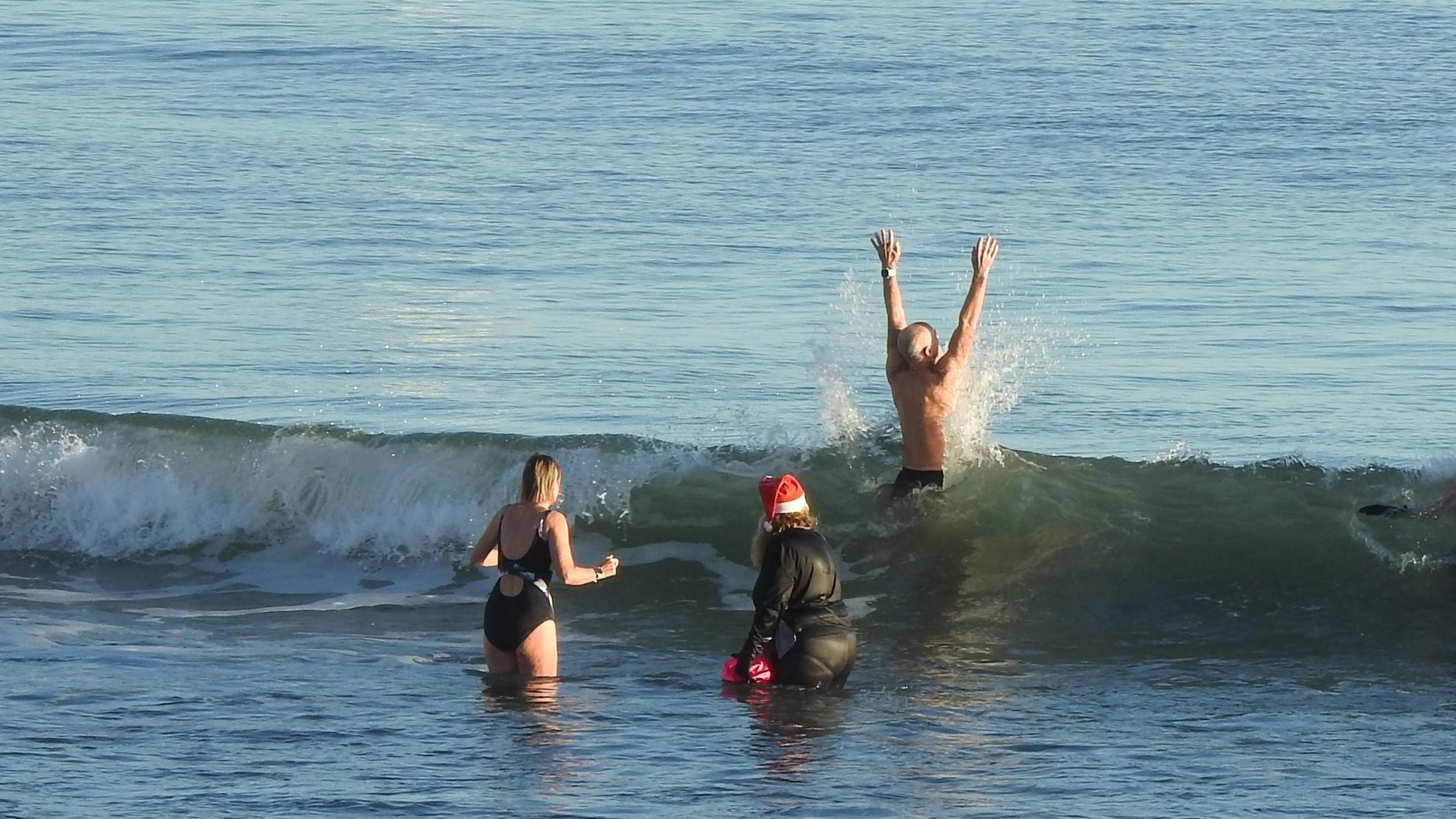 Three people are jumping through waves. ONe is wearing a sant hat, another has his hands in the air.