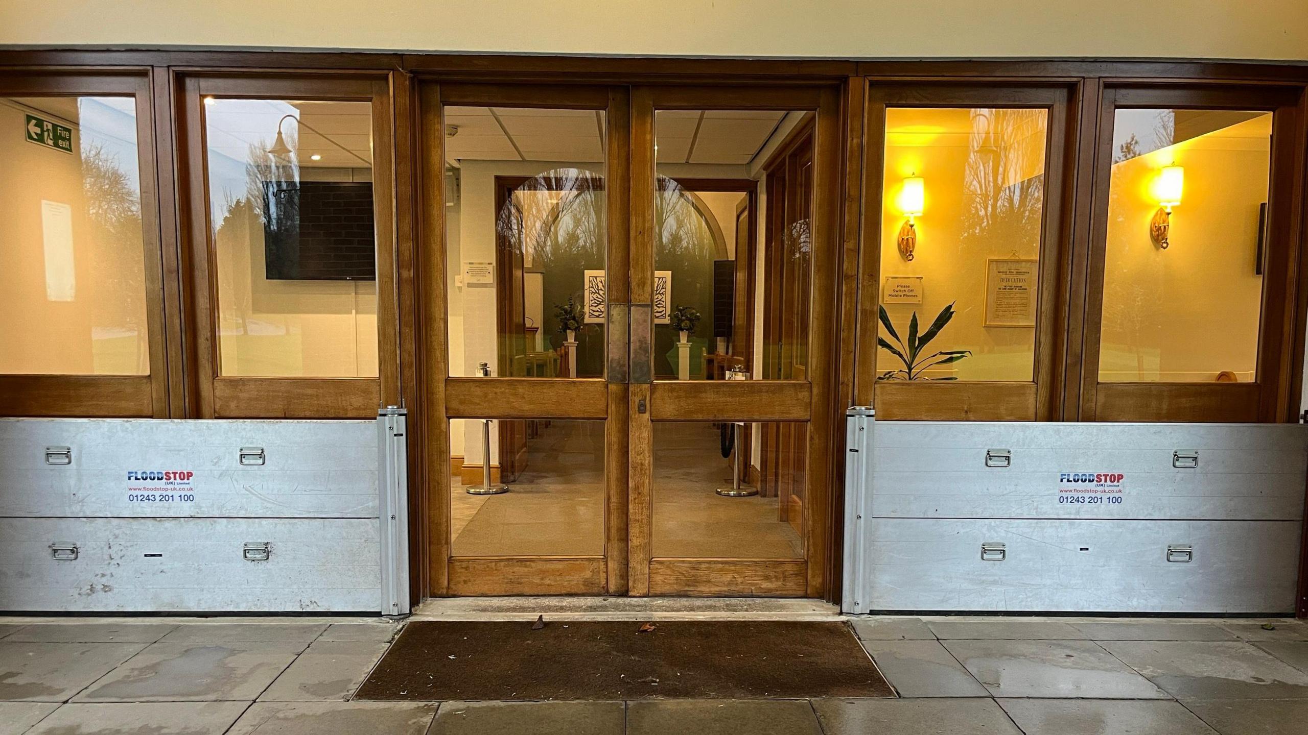 Brown external doors with glass panes. There are large metal panels in front of windows either side of the door