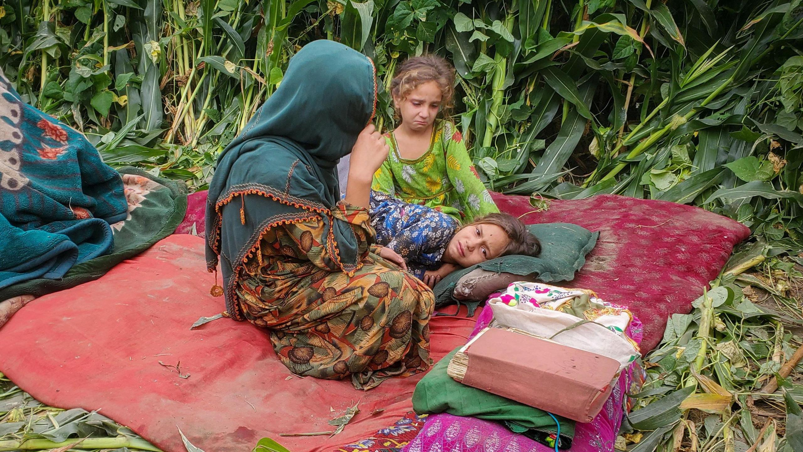 A woman and two girls, who are crying, sit on a mat
