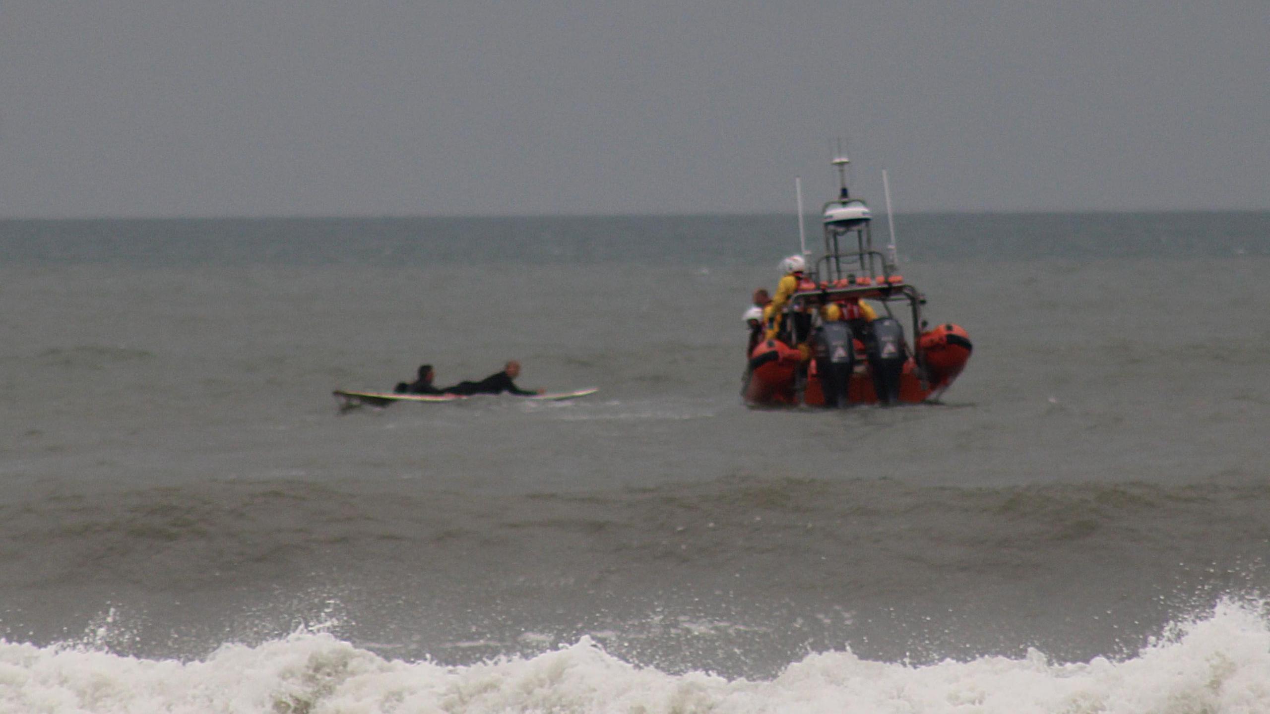 Oscar is manoeuvring the man on his surfboard towards the RNLI inshore lifeboat.
