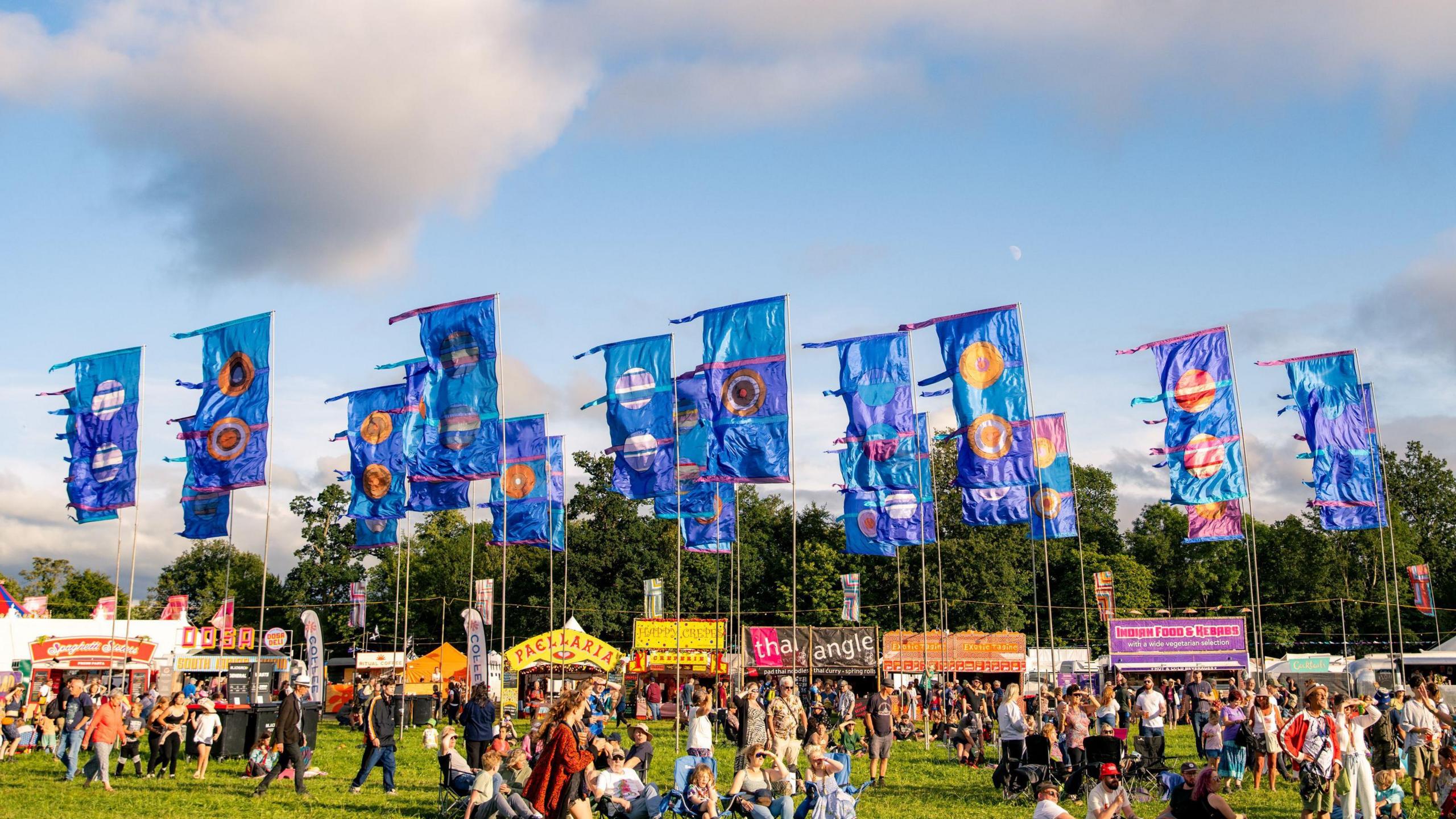 Festival scene with blue flags with multicoloured large circles on them and trailing tails