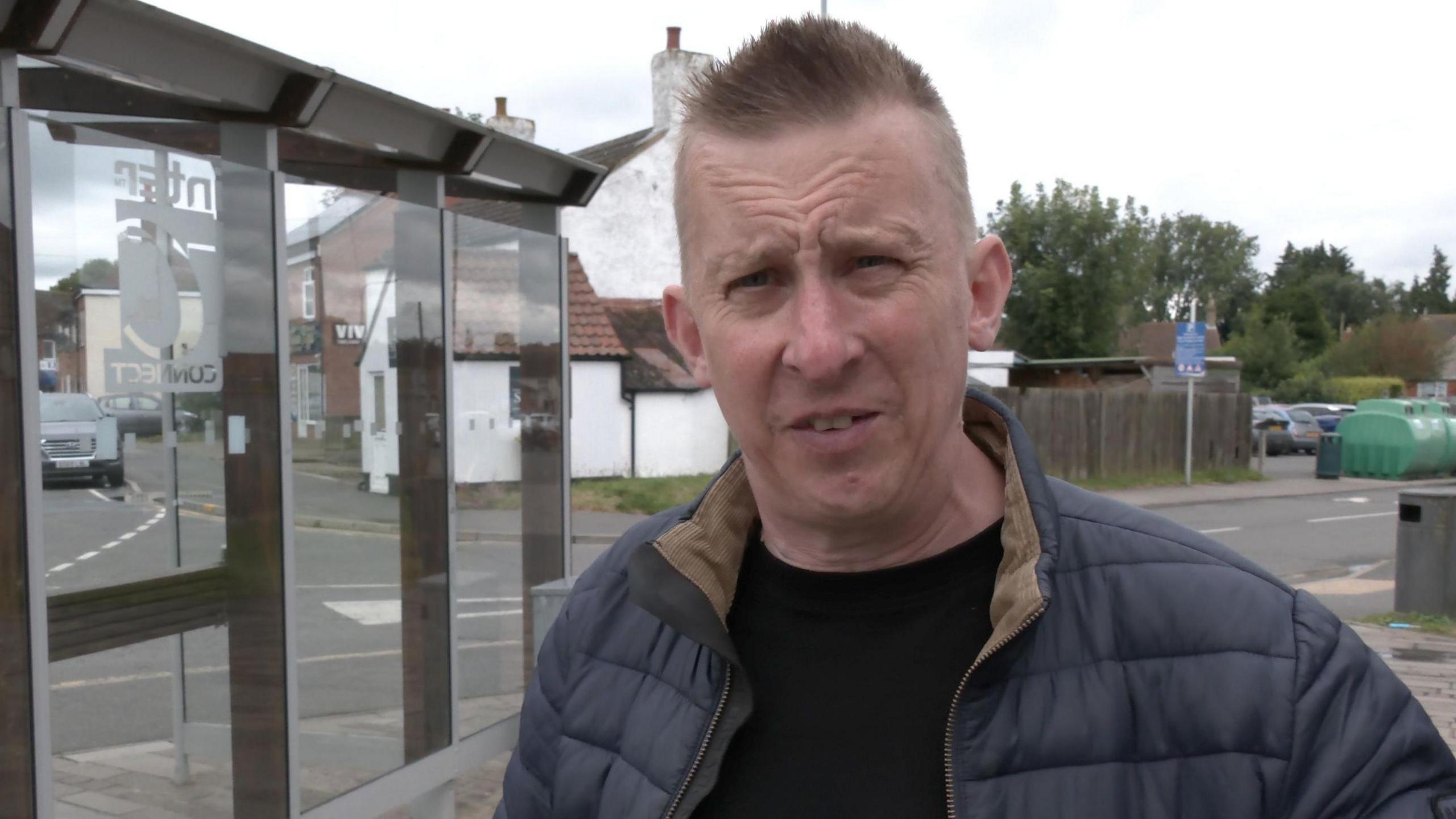 Simon Louden stood in front of a bus stop on an overcast day