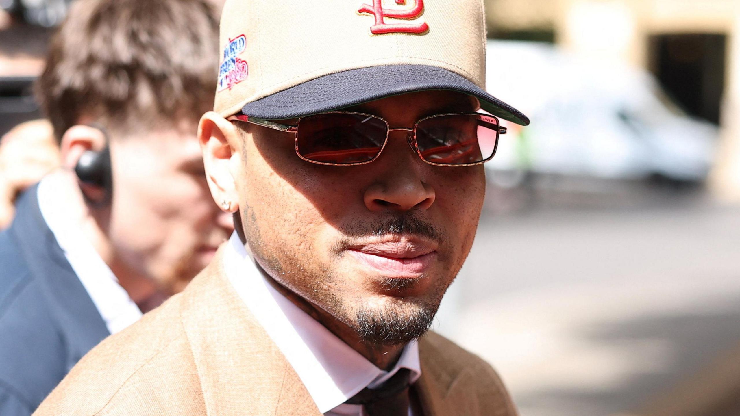 US singer Chris Brown arrives at Southwark Crown Court wearing a beige suit, glasses and a baseball cap