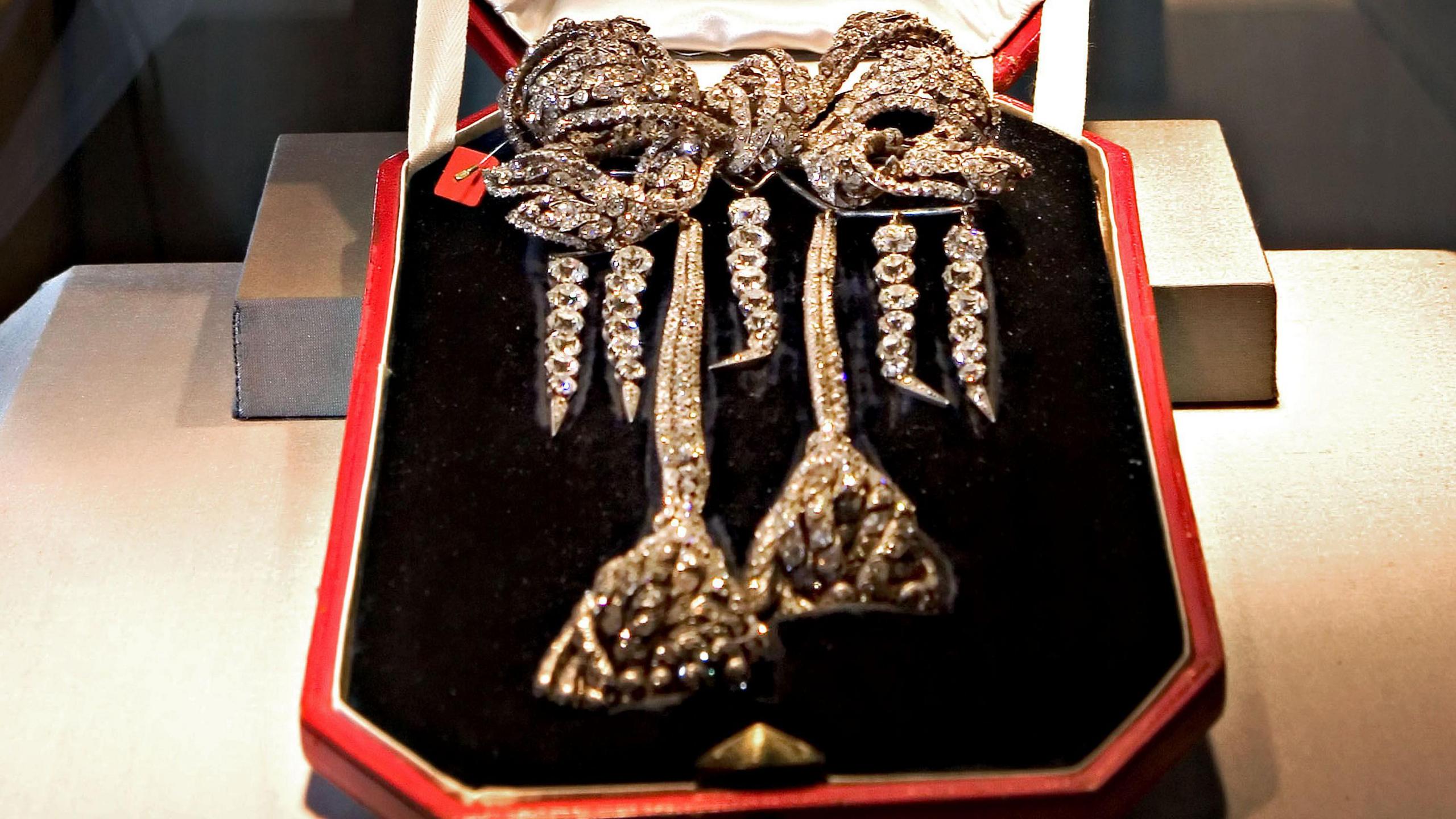 The antique Empress Eugenie Brooch, an antique diamond bow brooch, pictured in a black velvet box with a red exterior. It is a lavish bow shape with trailing strands of diamonds in the shape of two large tassels, and four further strands hanging from the bow