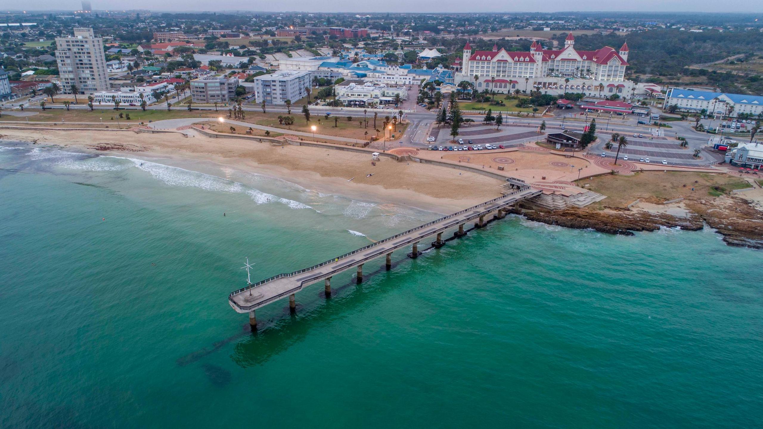 An aerial view of Shark Rock Pier in Gqeberha. The pier can be seen jutting out from the beach over a clear ocean.