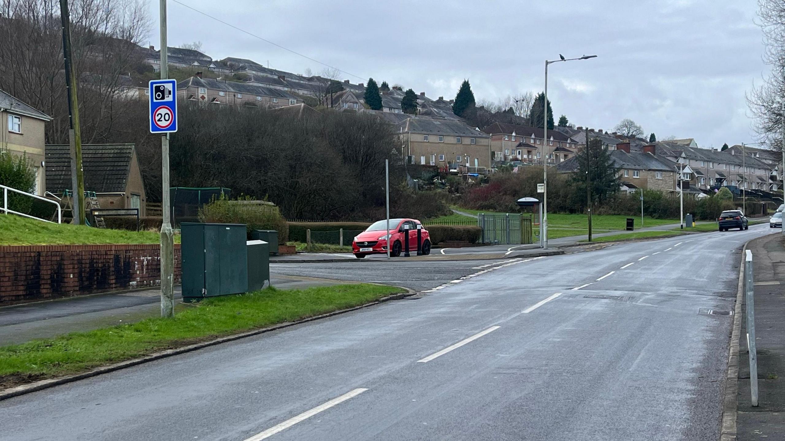 A section of Gors Avenue, with houses and parked cars in the distance, and a 20mph and speed camera sign in the forefront