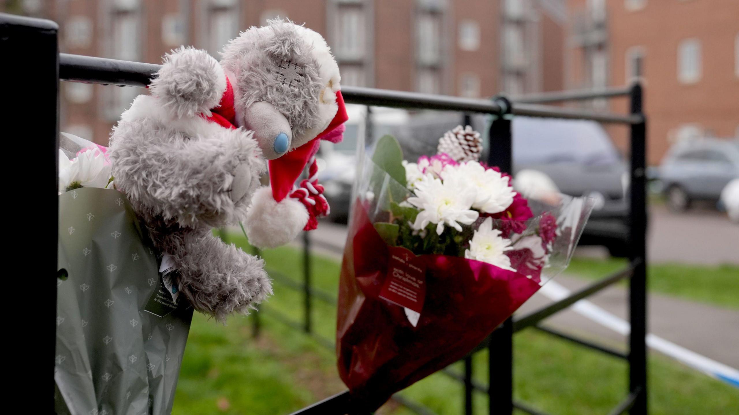 A floral tribute and teddy bear are tied up on a railing in a residential estate.