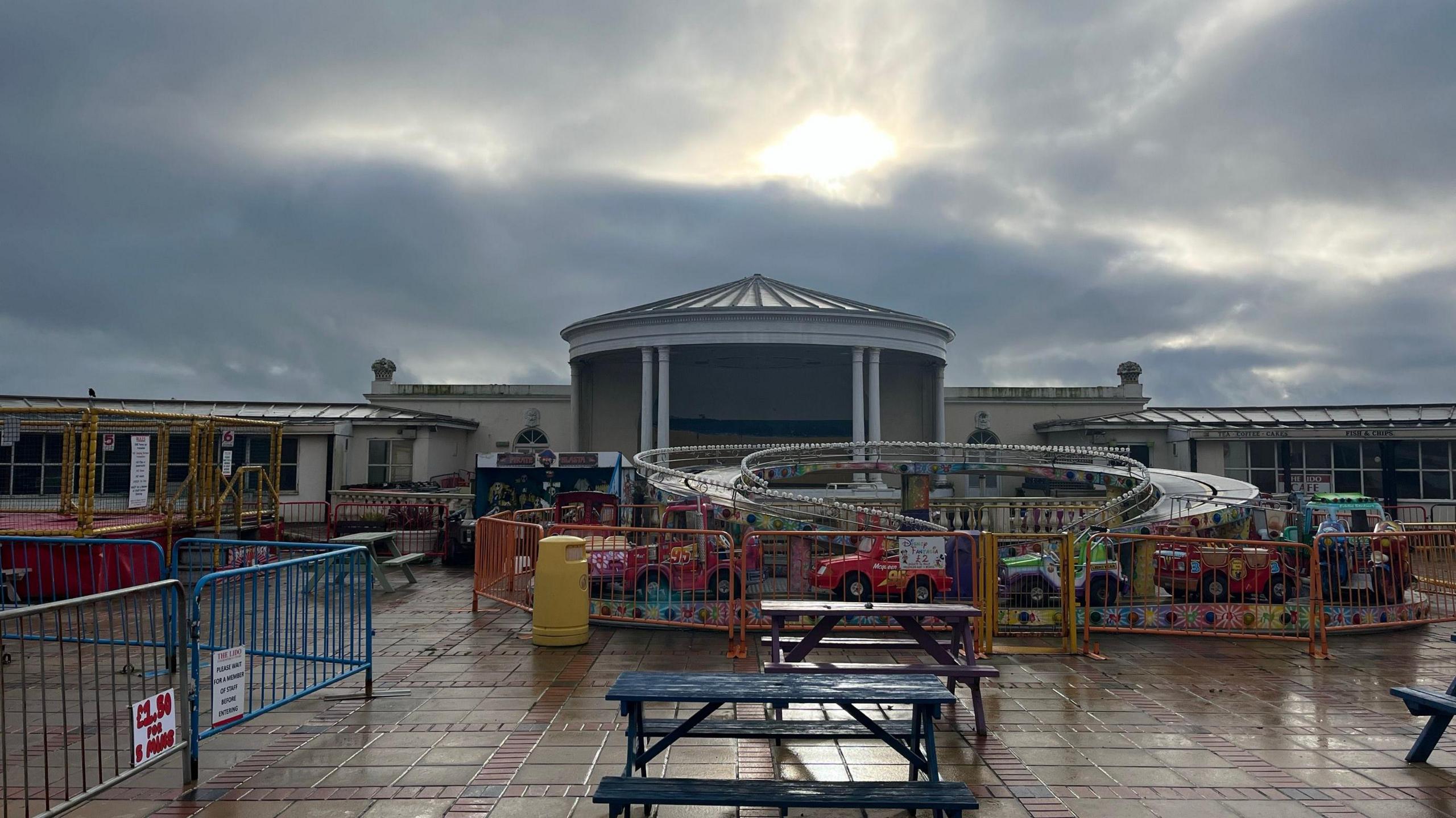 The area where the pool used to be which is now filled with children's amusement rides. To the left are trampolines, a mini-roller coaster in the middle and the bandstand can be seen behind. The rides are all closed because it is winter season