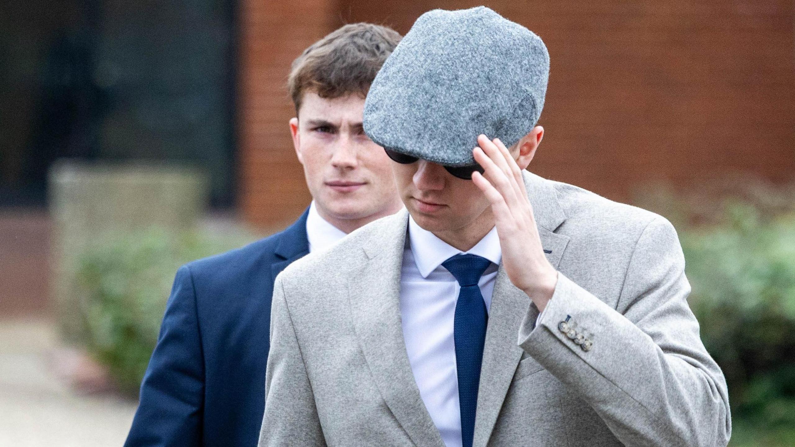 Two young men both seen wearing suits. One has a flatcap covering part of his face and is also wearing sunglasses. The other's face can be seen clearly.
Daniel Heath is seen on the right in a blue suit with his face uncovered - William Lawrence is seen on the left with a grey suit and blue tie.