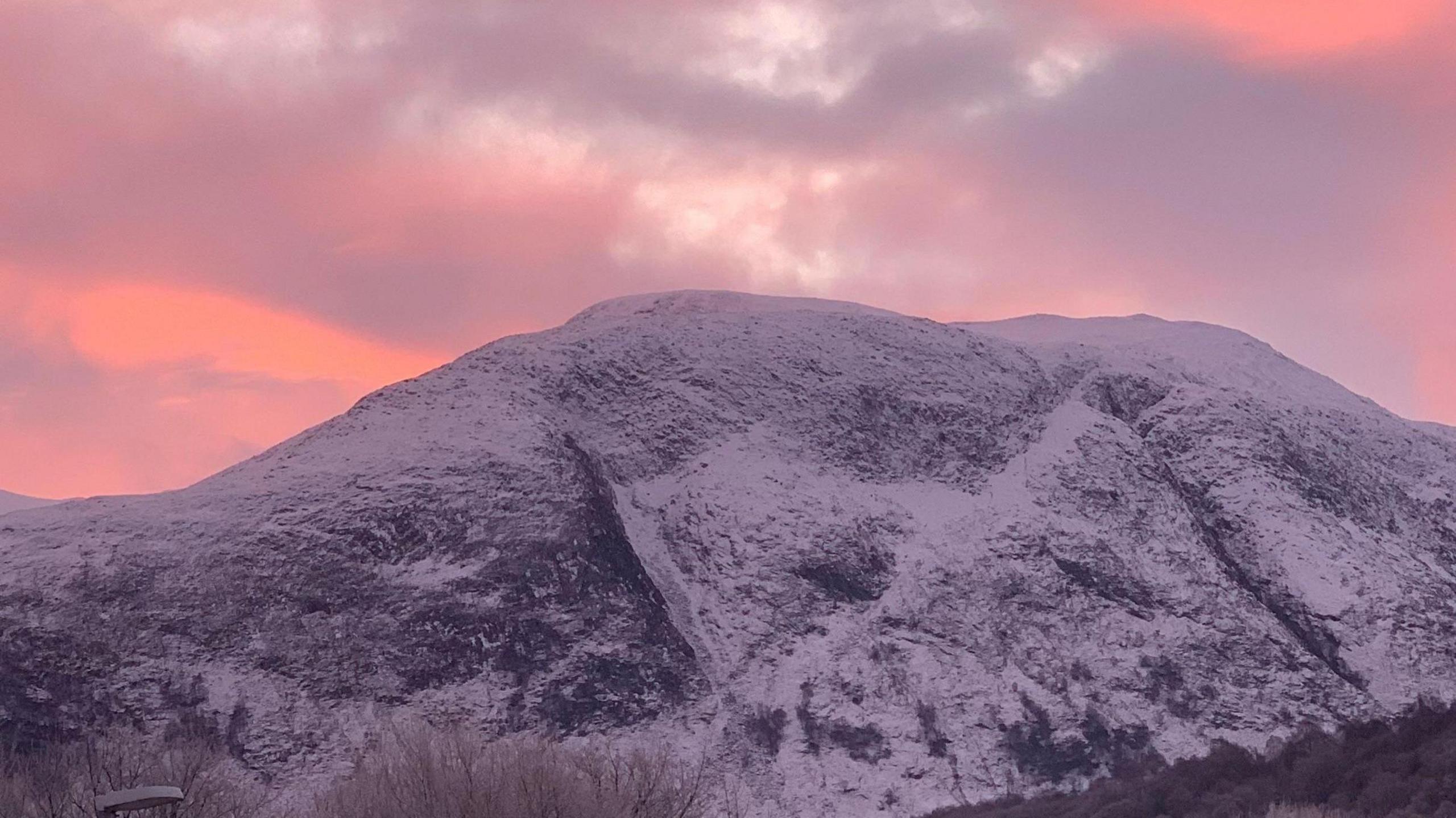 A snow covered mountain against an orange and pink sky