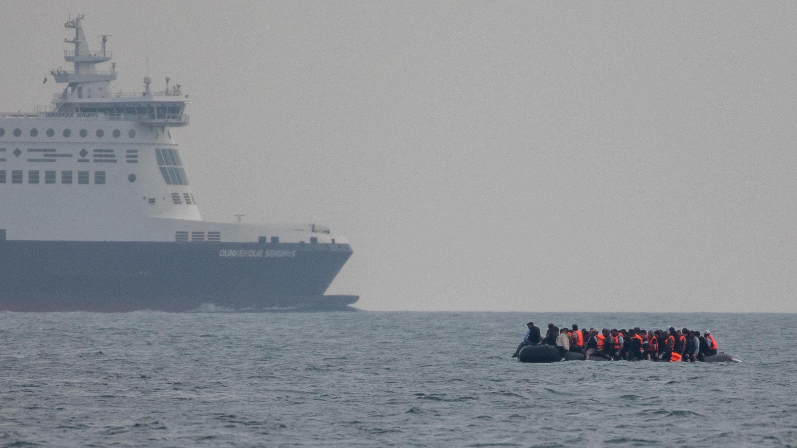 An inflatable dinghy in the English channel carrying people wearing life jackets, seen as it nears a passenger ferry 