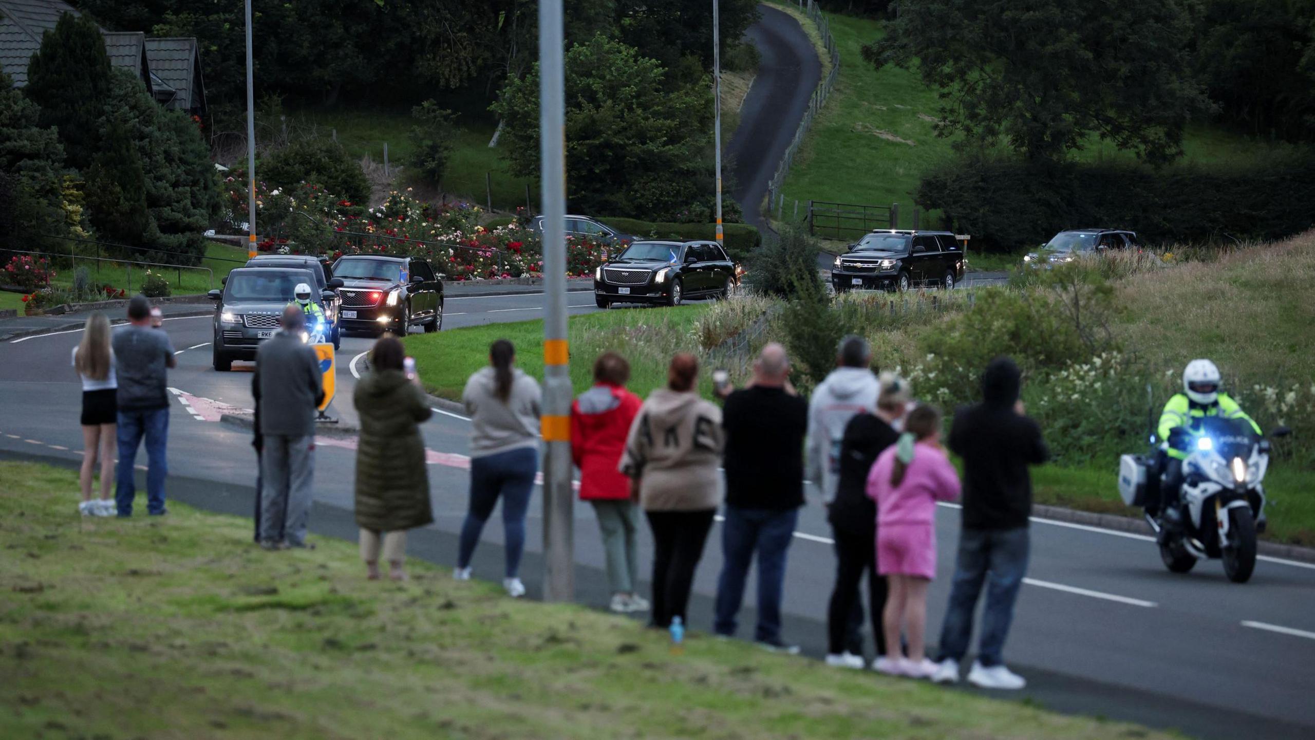 A dozen people stand at the side of the road as the Trump motorcade makes its way to Turnberry. 