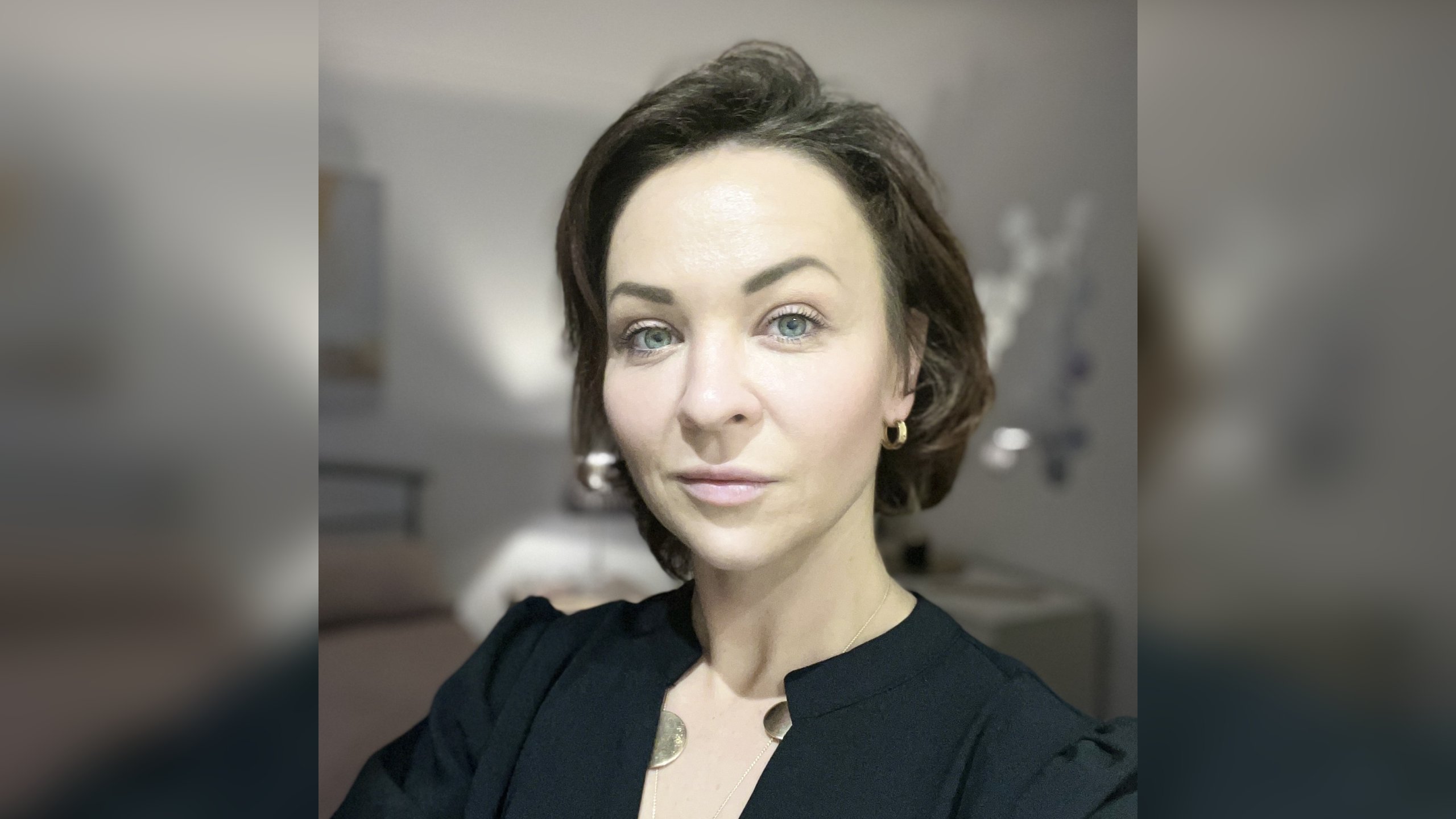 A woman with short brown hair and a smart black top looks at the camera. 