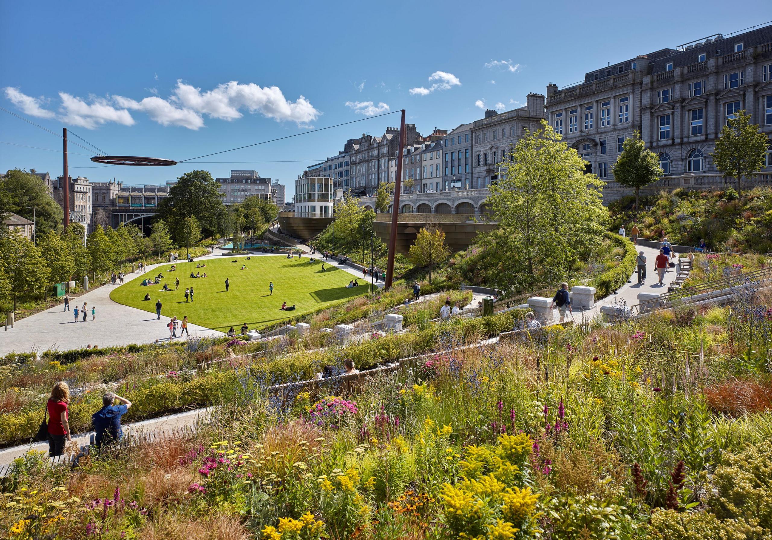 A view of Union Terrace Gardens showing the stunning plant arrangements, a grassy area in the centre and people walking around enjoying the space.