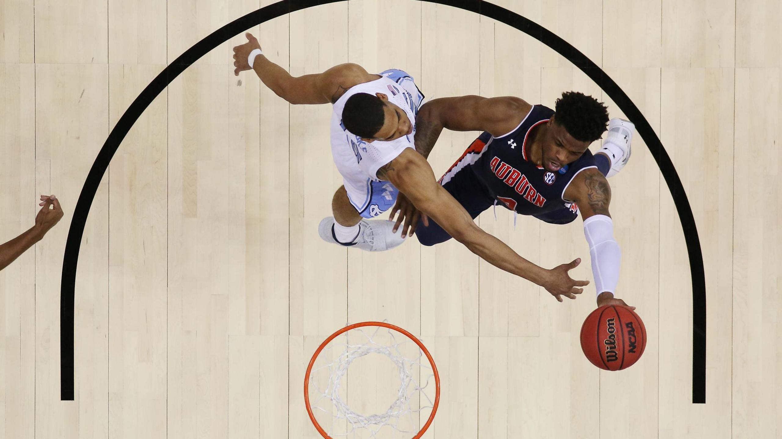 Malik Dunbar attempts to score a lay-up while playing for the Auburn Tigers. The camera view is above the basket, looking head down at Dunbar, in blue, and his opponent, in white, who is trying to stop him. 