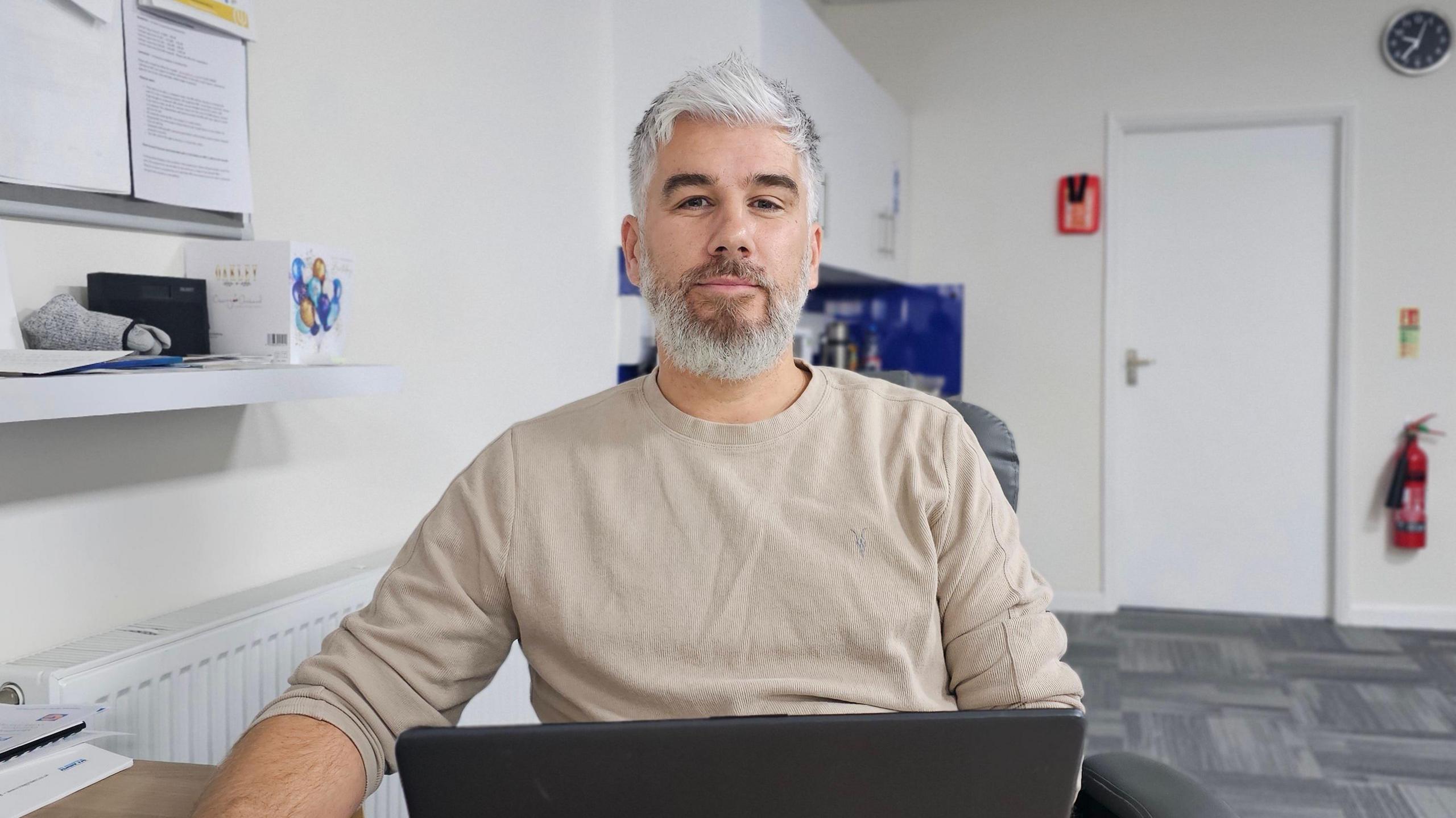 Chris Gibbons sitting in his office, with a laptop in front of him.