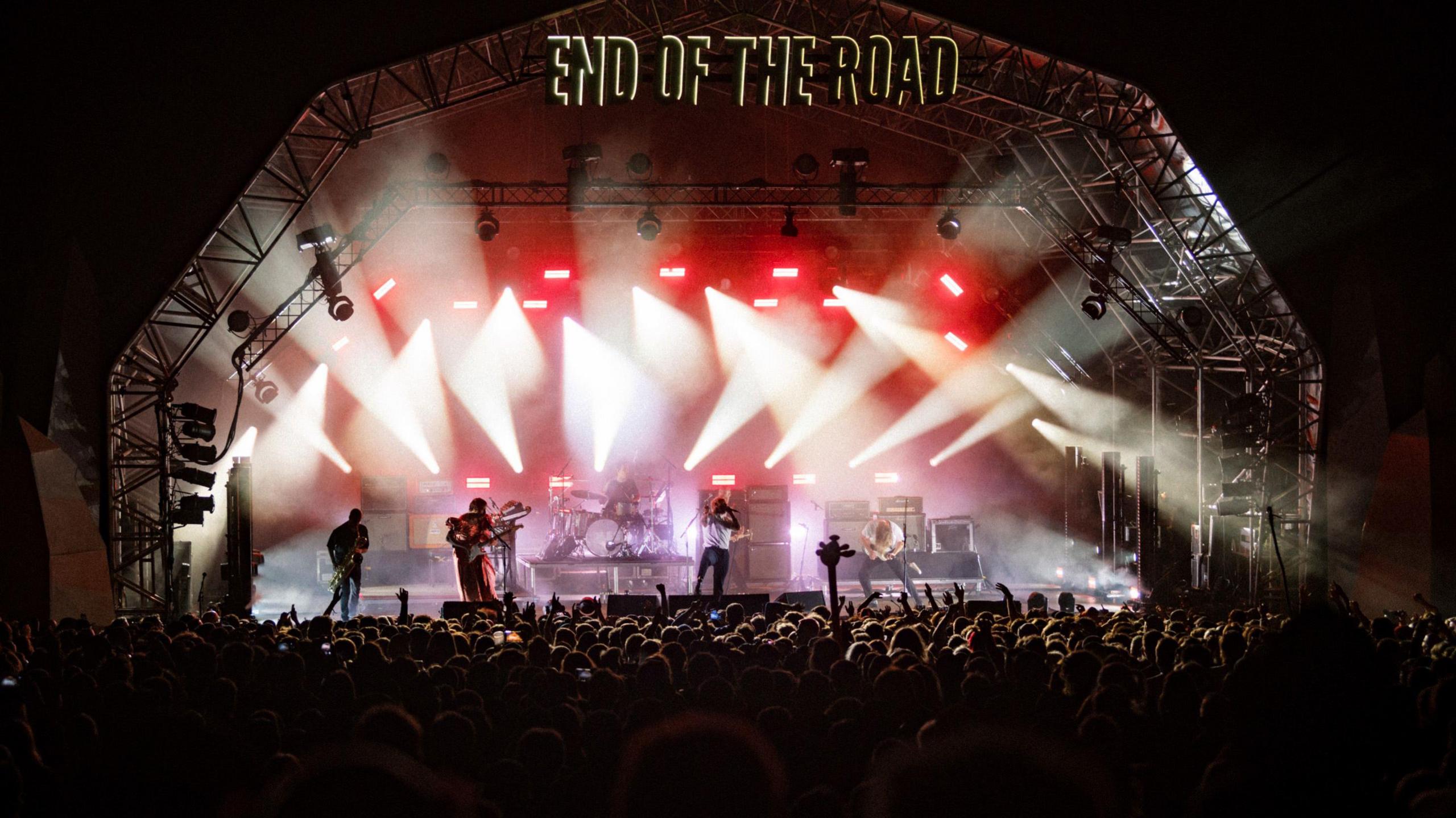 The festival stage at night. A band is performing under red and purple lights and the crowd stands in front of their stage with their back to the camera.