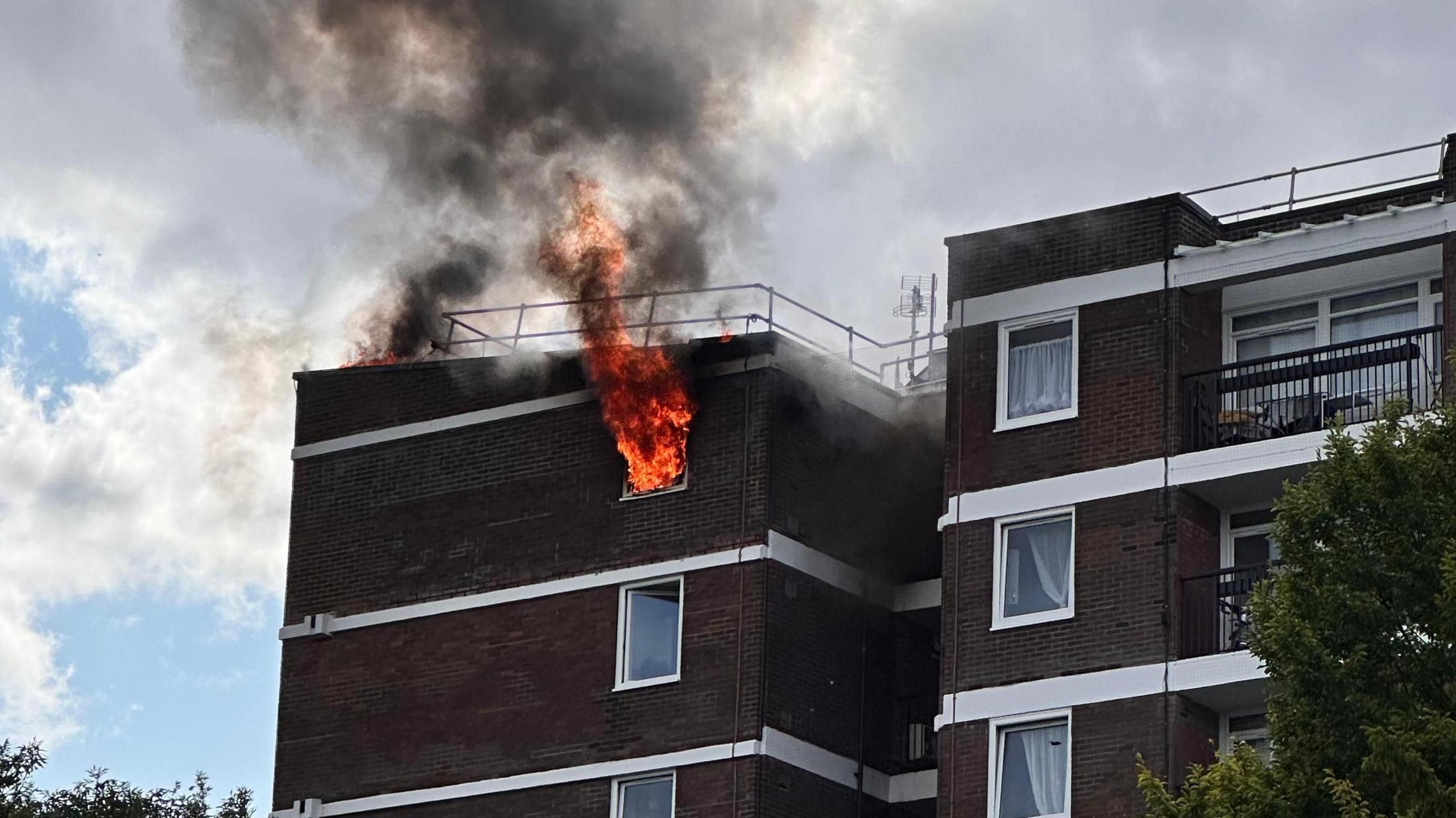 Fire pours out of a window at the top floor of a block of flats