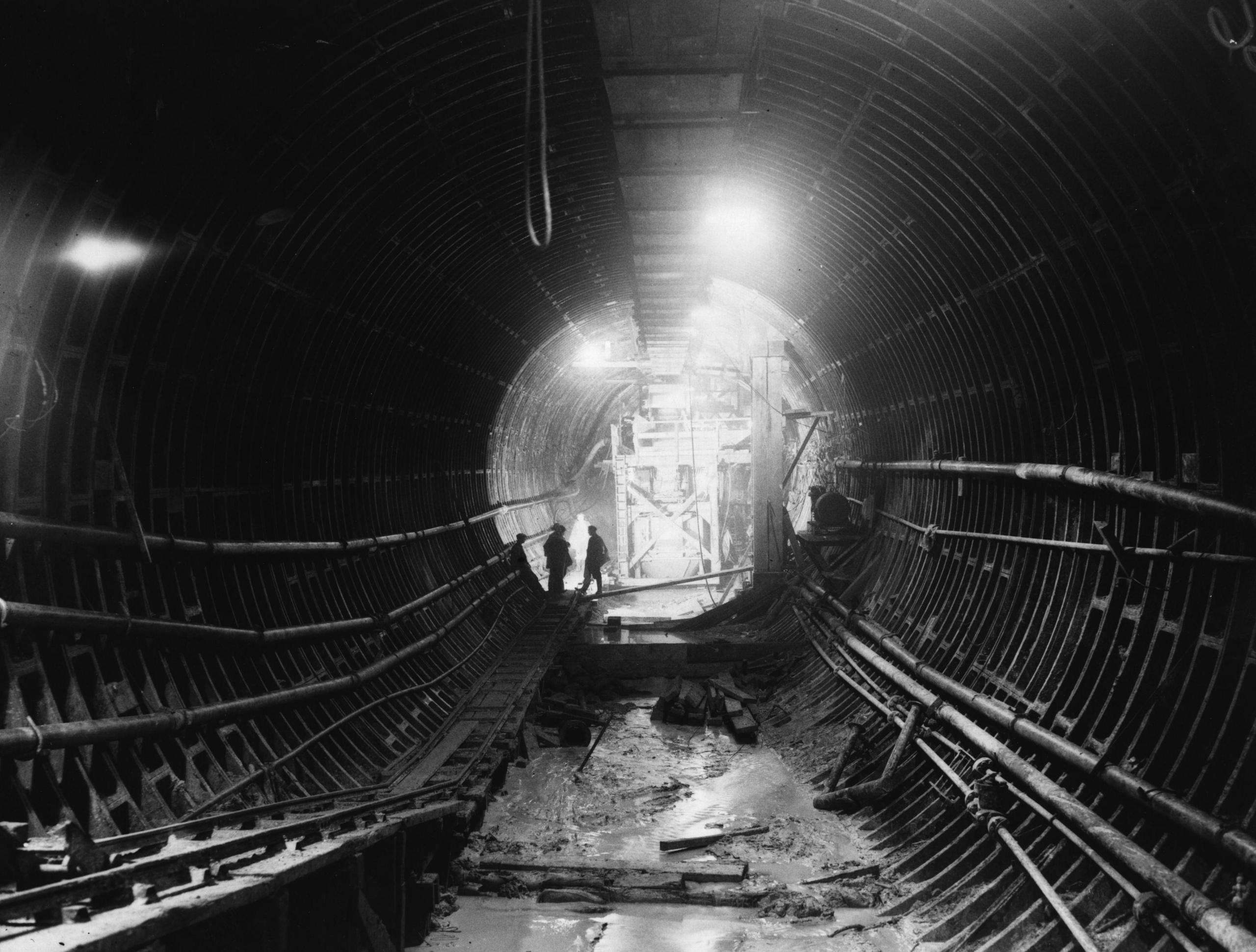 The image shows two construction workers silhouetted in a section of tunnel during the building of the Dartford Road Tunnel. (1959)