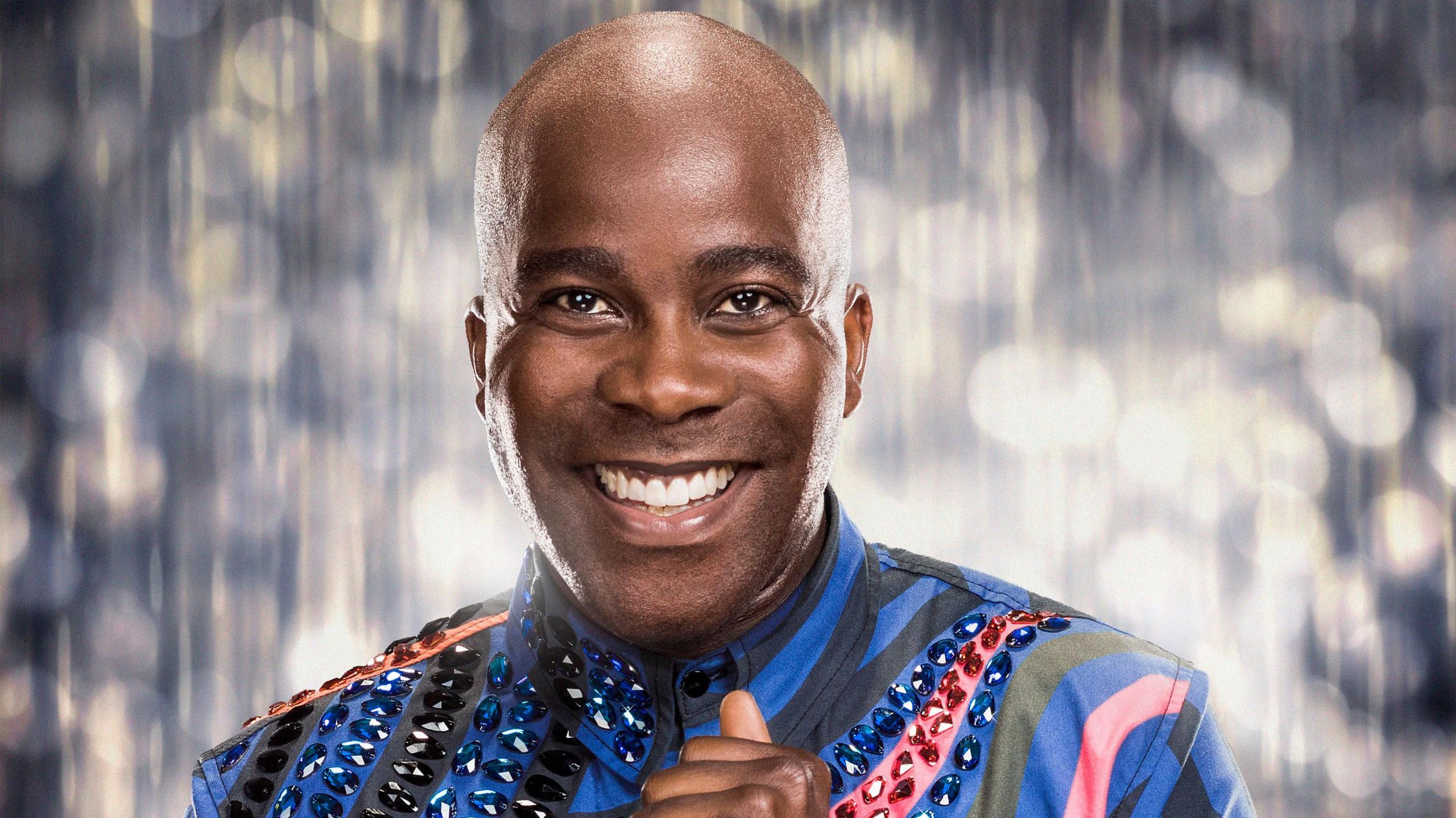 Melvin Odoom smiling while wearing blue and black shirt with gems embedded into it