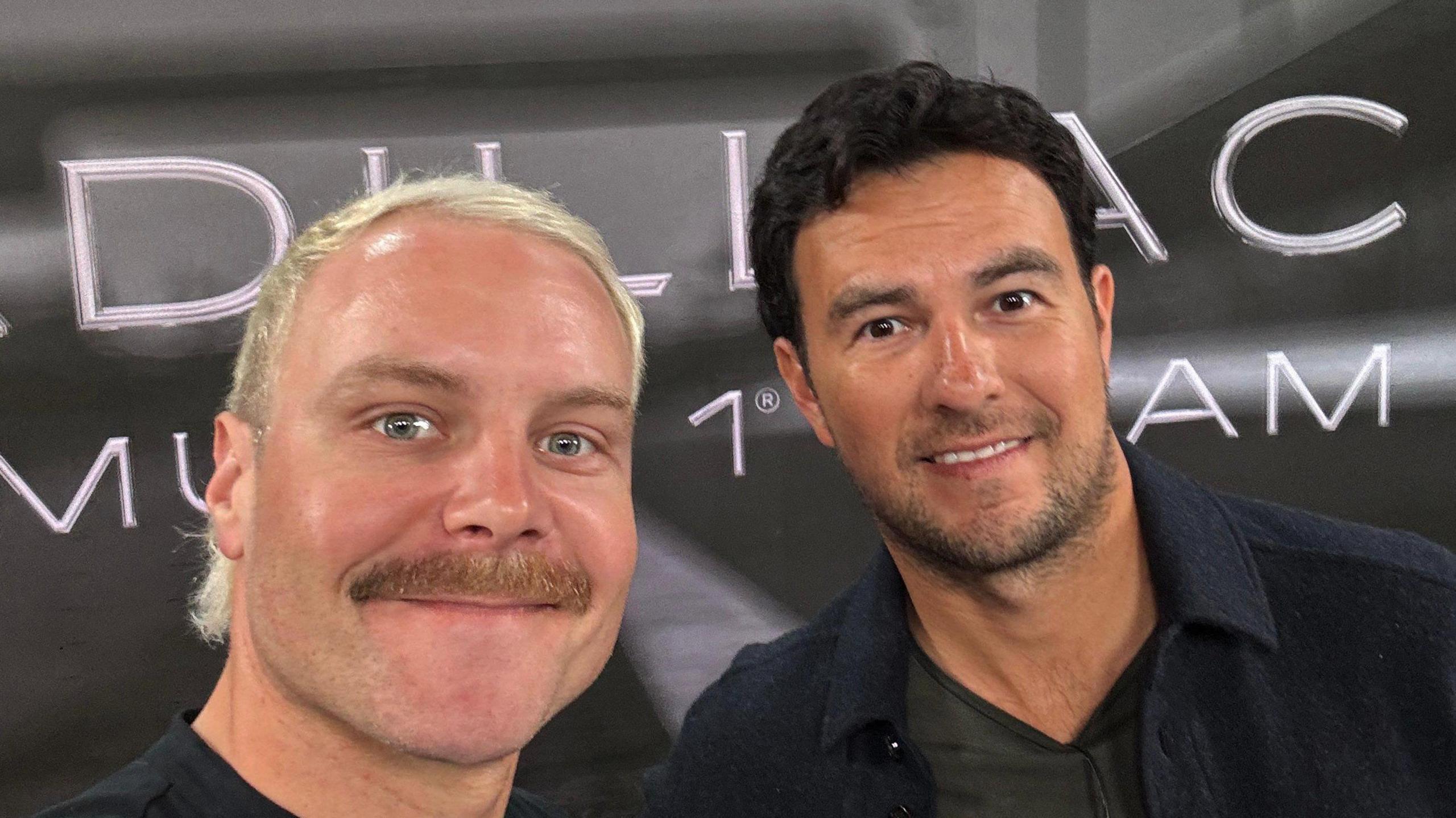 Valtteri Bottas and Sergio Perez take a picture in front of the Cadillac sign 