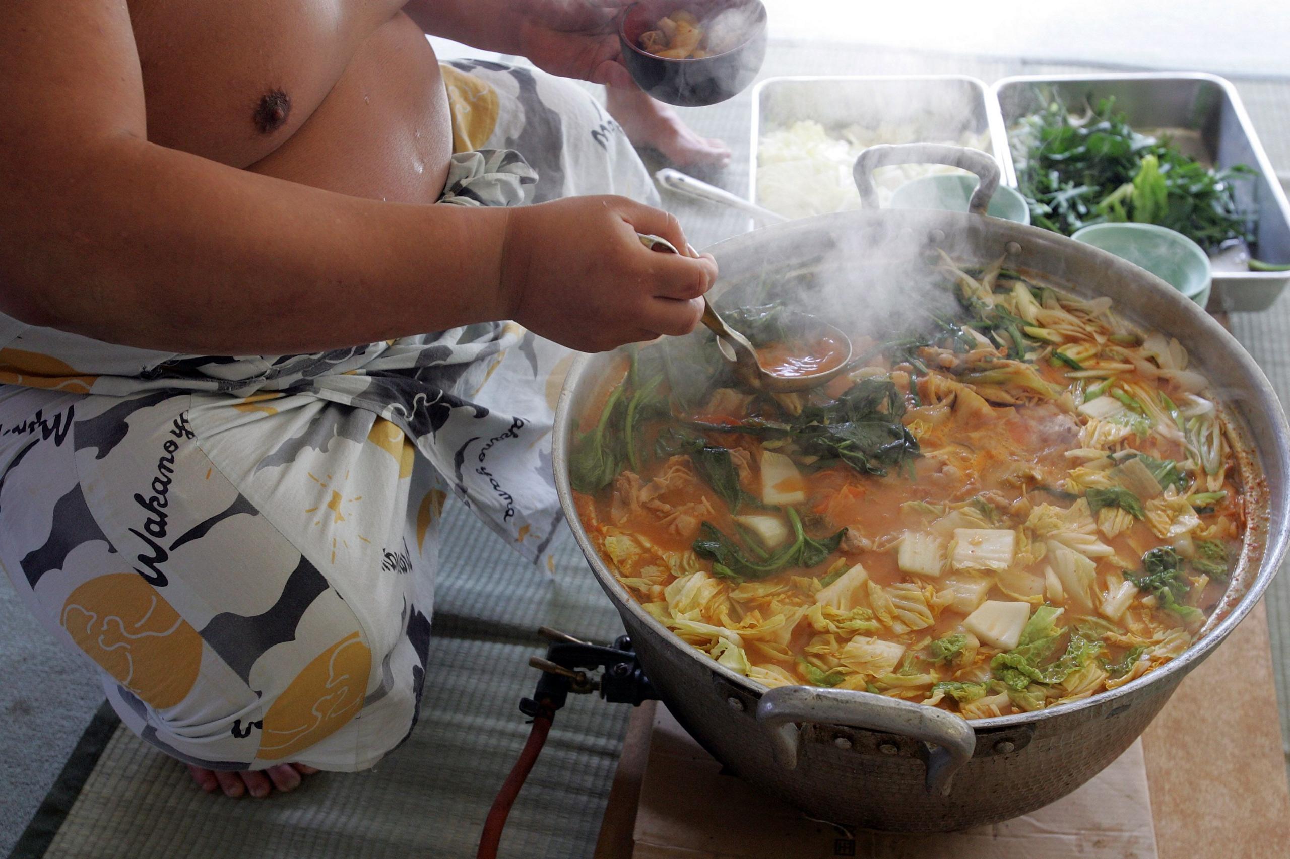 A sumo wrestler is serving out of a large pot of stew at a sumo stable