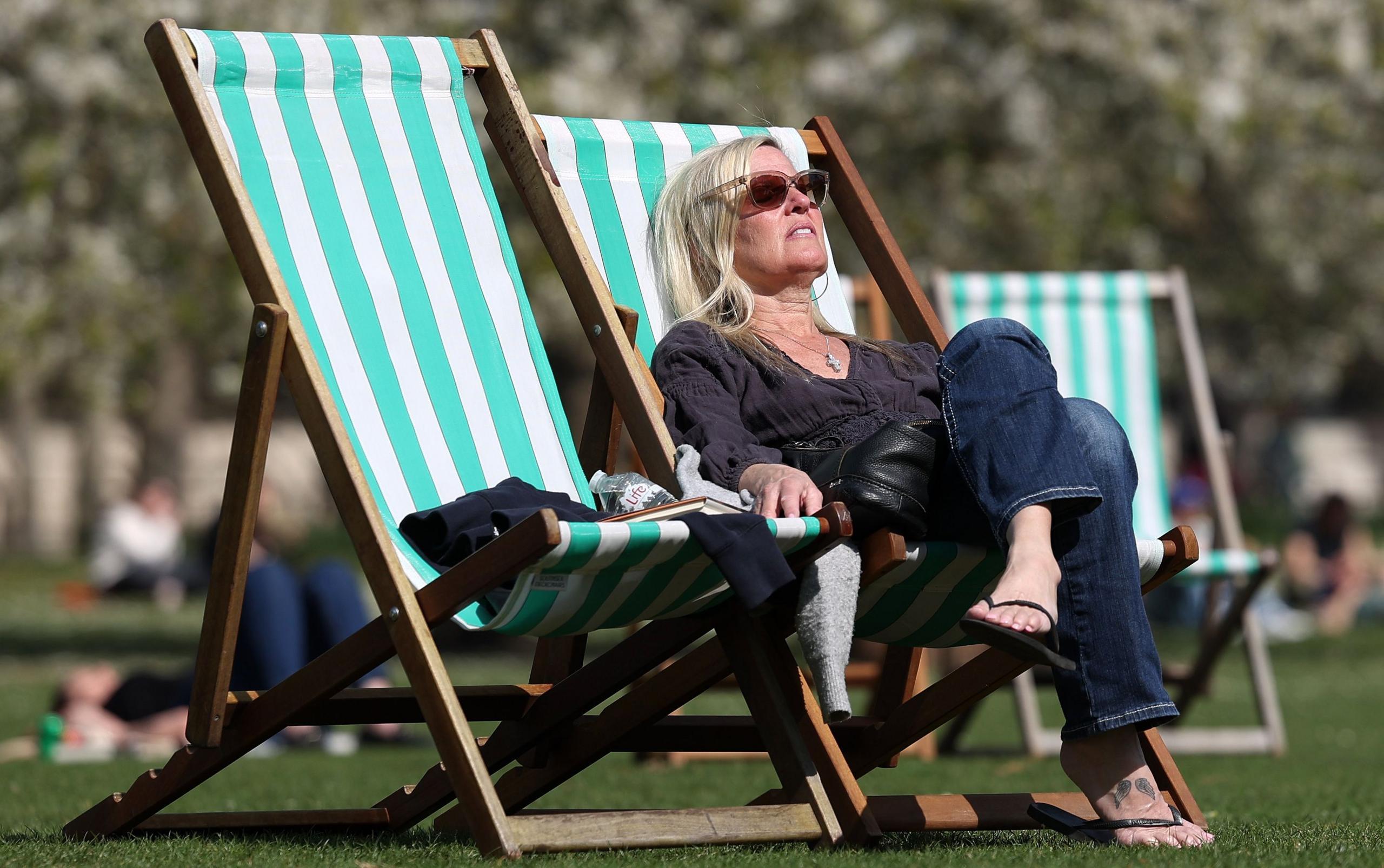 A woman sunbathes on a striped deck chair in a park