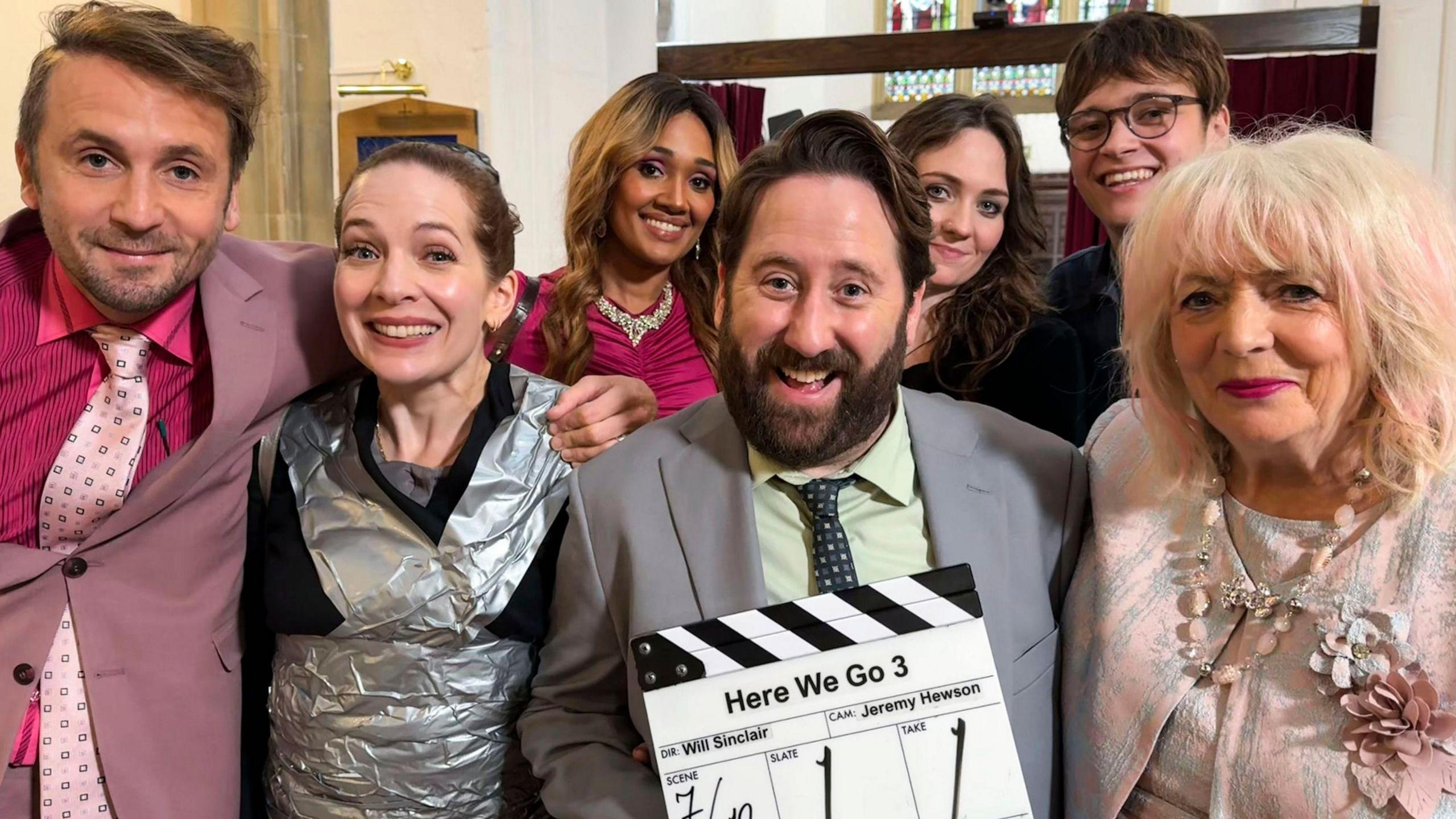 A group of actors from Here We Go standing together with a clapperboard labelled “Here We Go 3”