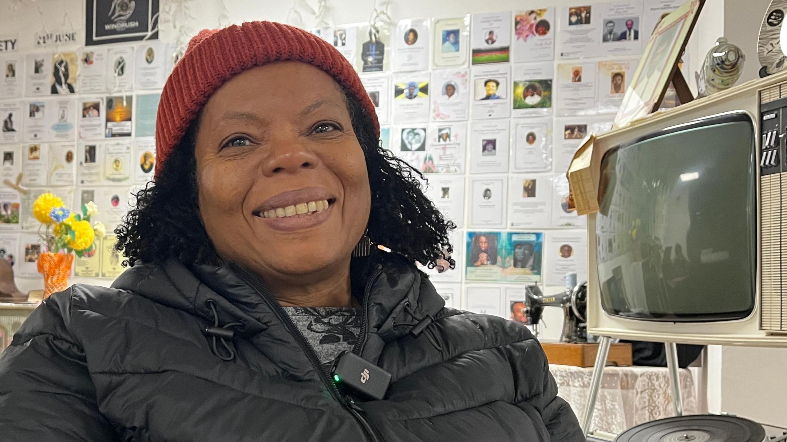 Ivya Scott with a red hat sits in front of a Windrush display