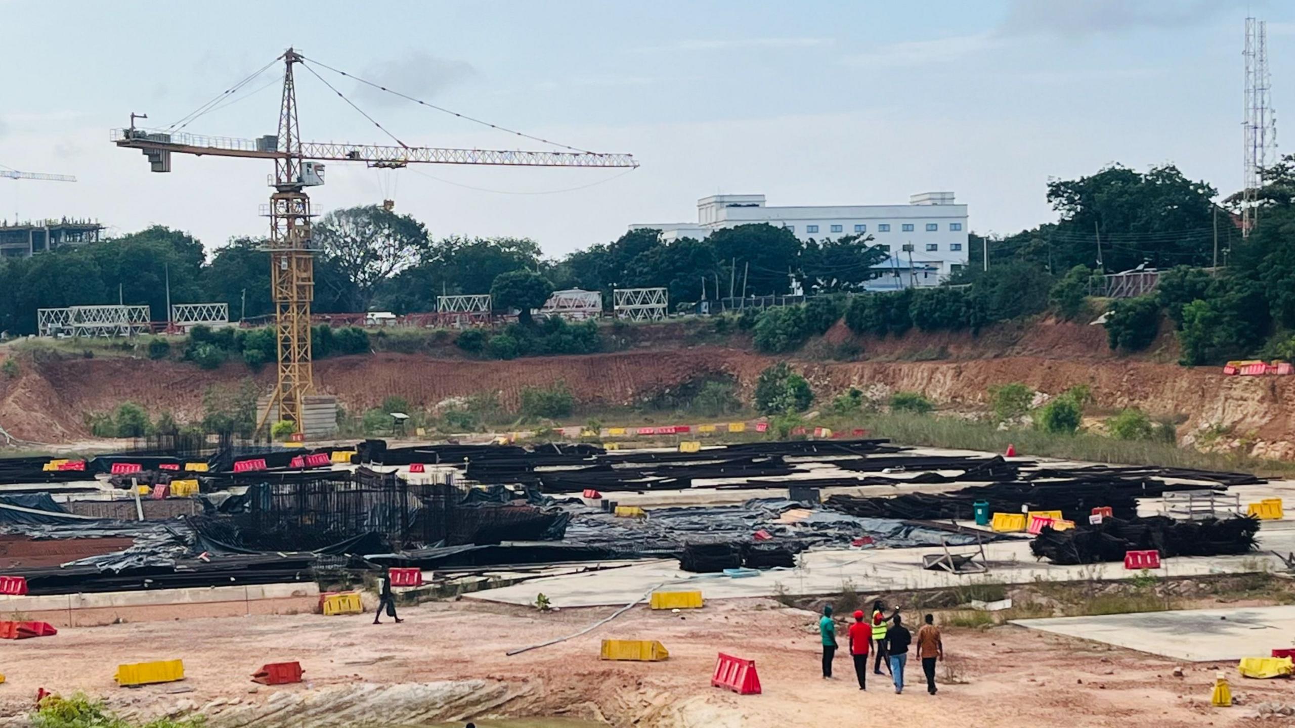 Six individuals walk on a construction site. A crane towers above them.