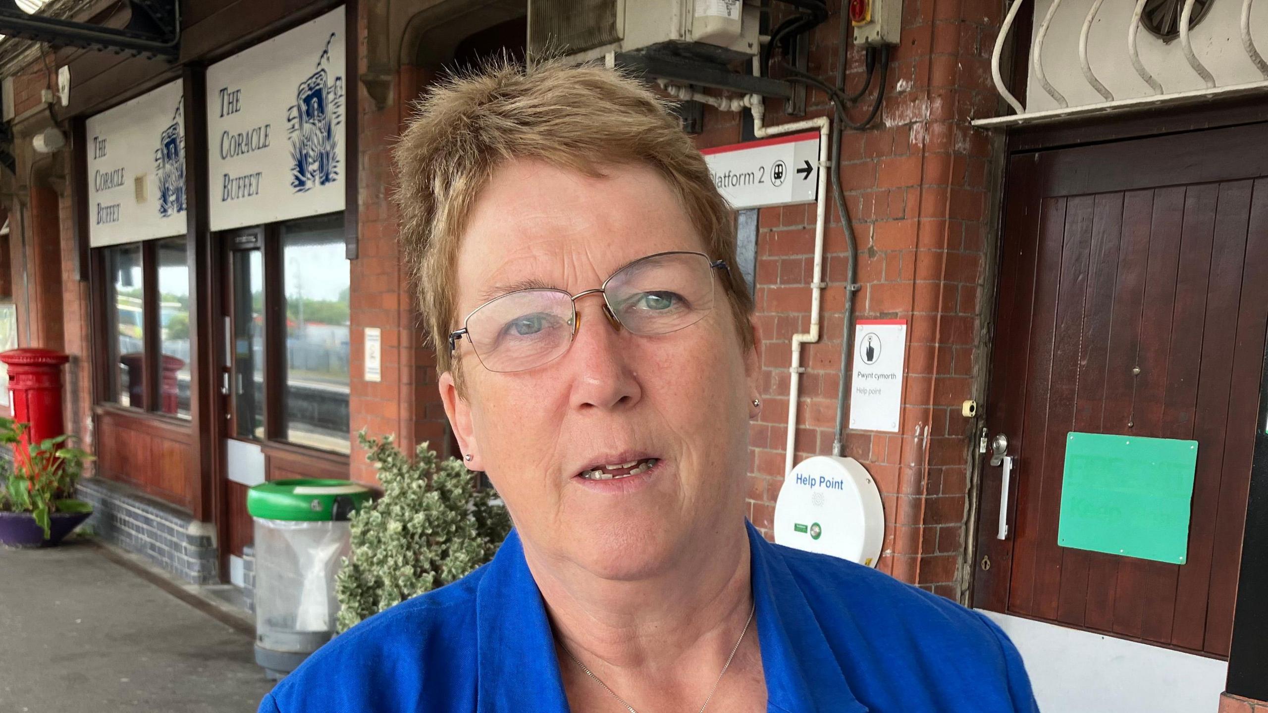 Ann Davies who has short light brown hair and glasses and is wearing a blue blazer