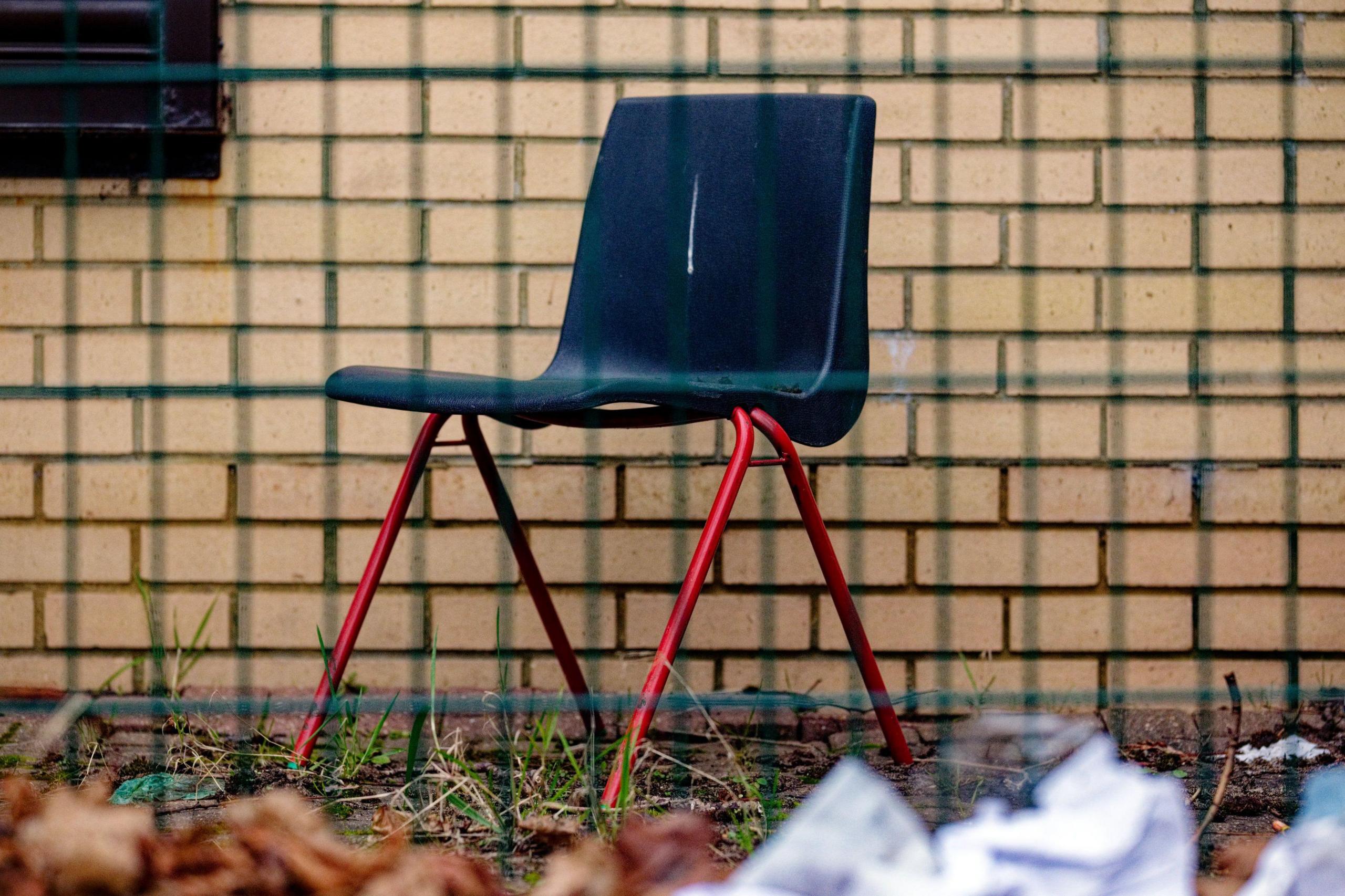 A lone chair outside the back of Broad Green library. There is a line of bird poo down the back rest of the chair and litter in front of it.