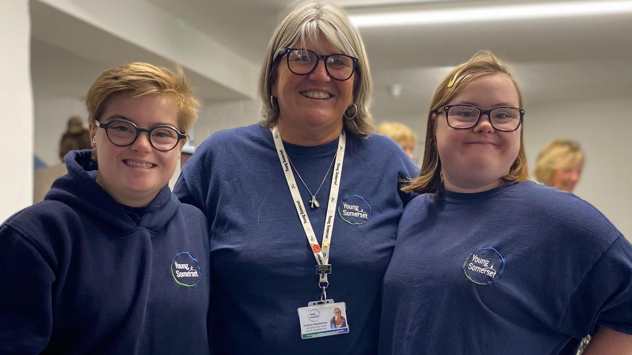 Lexie, Justine, and Charley are smiling at the camera.  They are wearing dark blue hoodies and t-shirts with Young Somerset written on them.