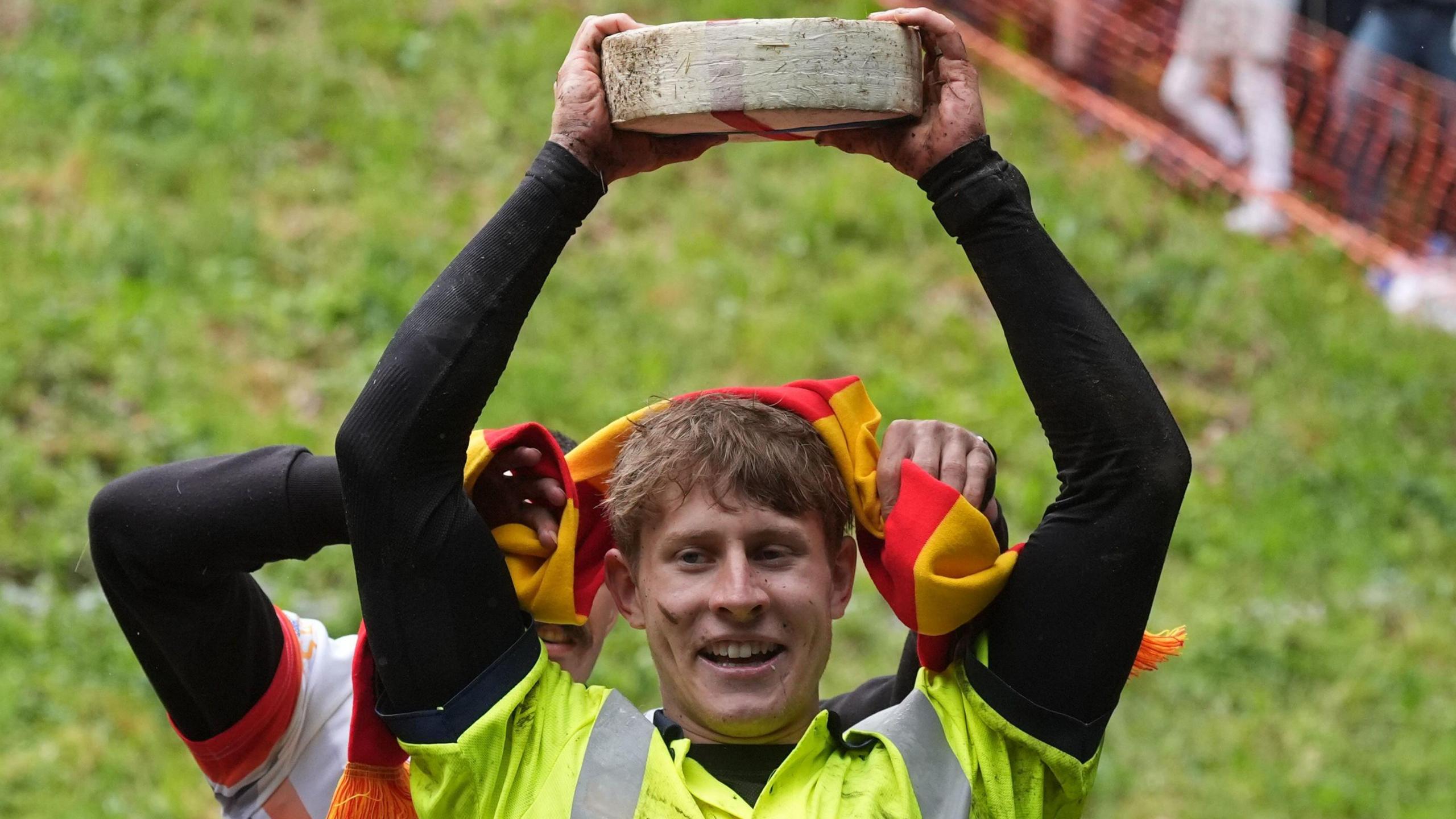 A man holding a wheel of cheese above his head