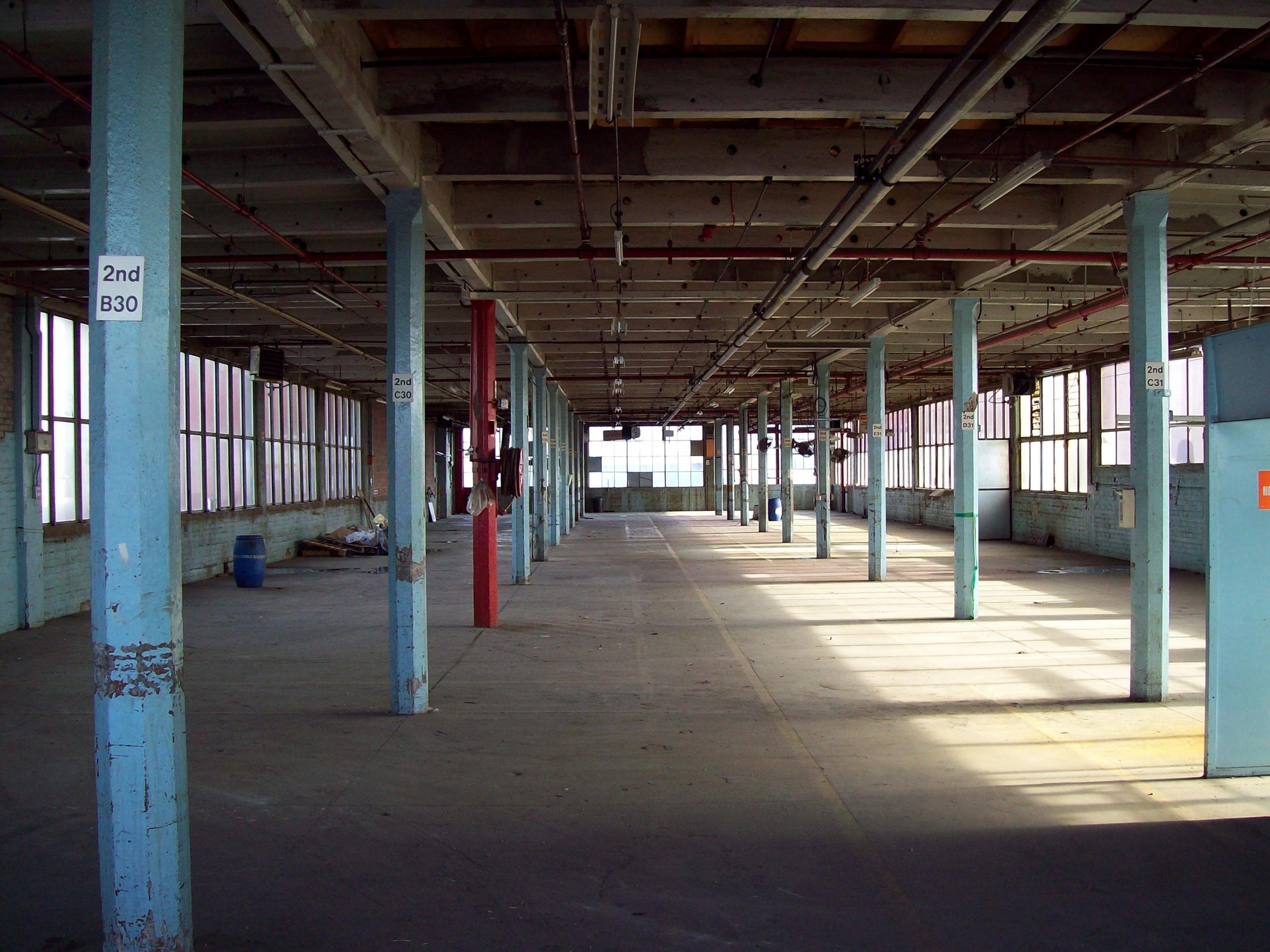 A factory interior with light spilling in from the right hand side and a long alleyway of metal pillars