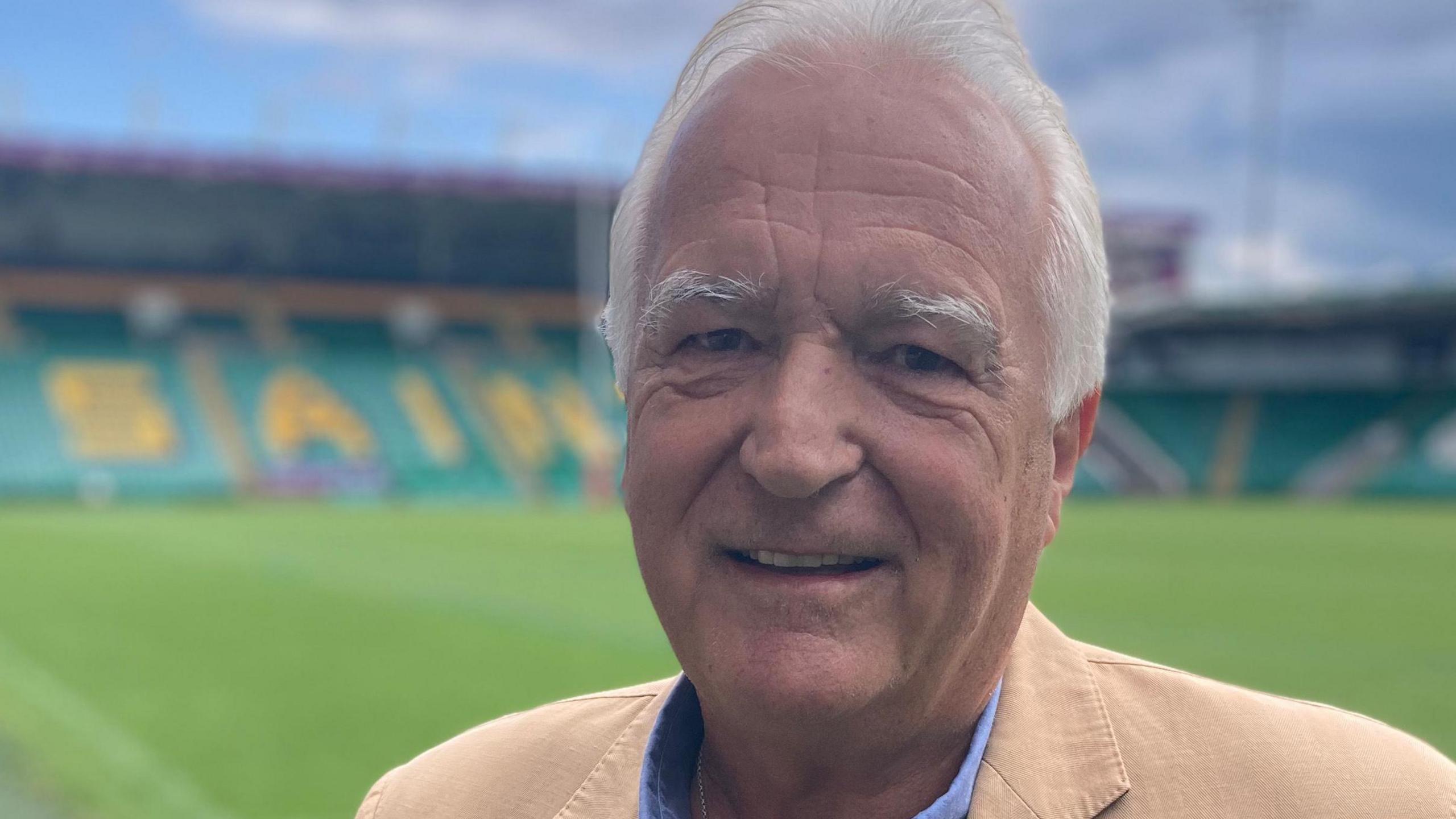 John White with short white hair wearing a beige jacket at the county ground