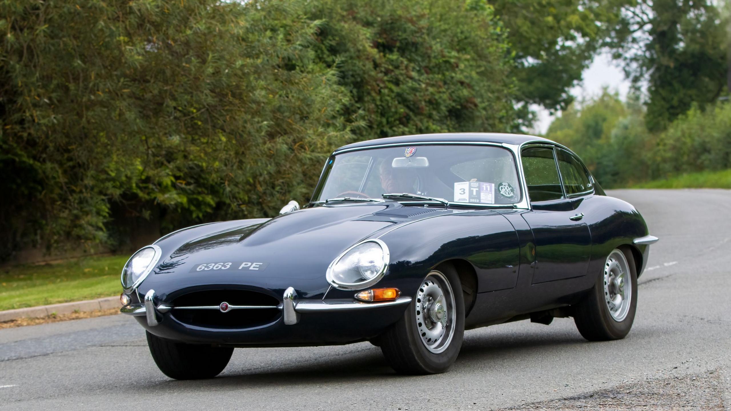 A Jaguar E-Type being driven on a country road